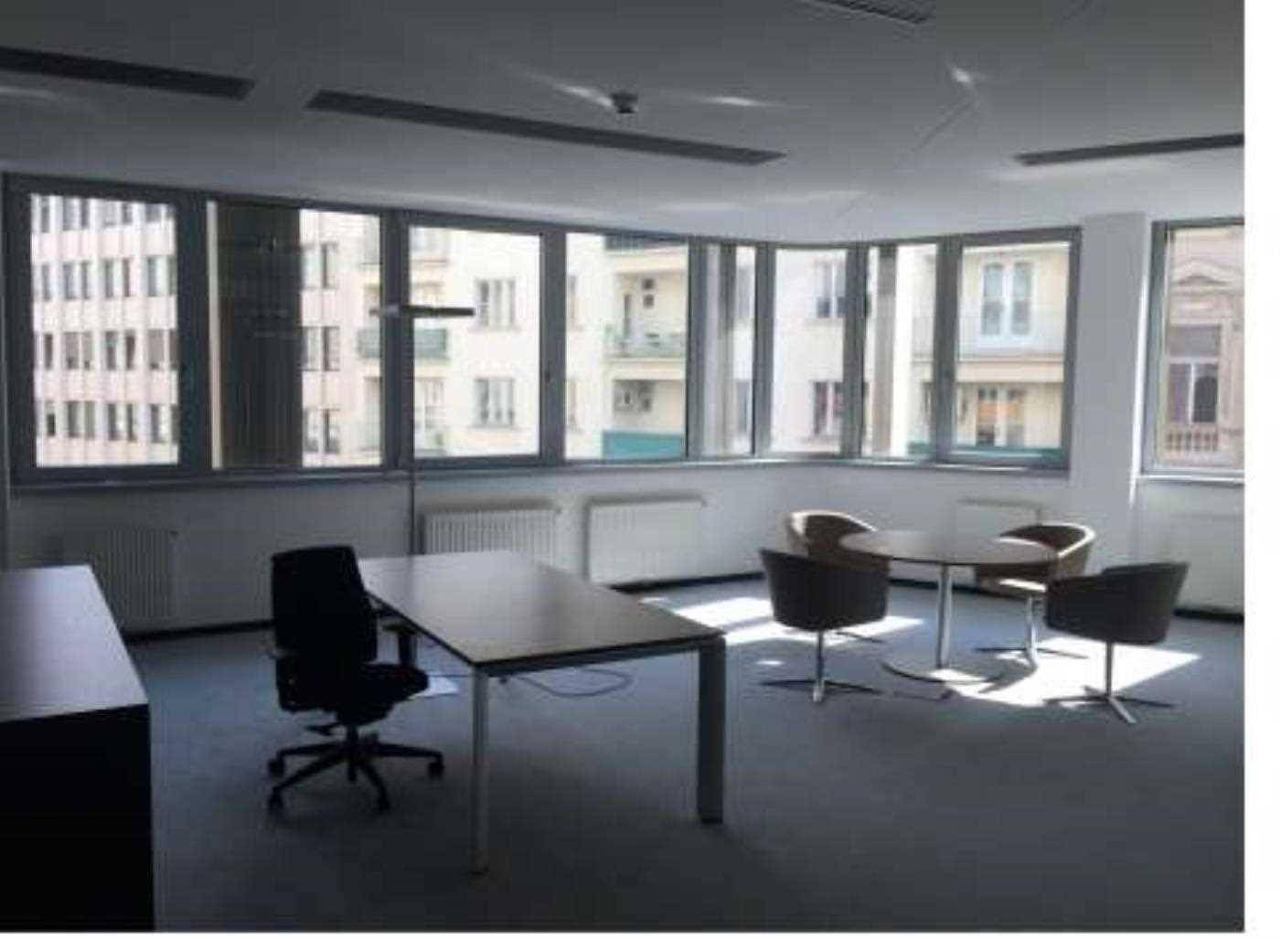 Leerer Büroraum mit einem Schreibtisch, Stühlen und großen Fenstern, die viel Tageslicht hereinlassen.
