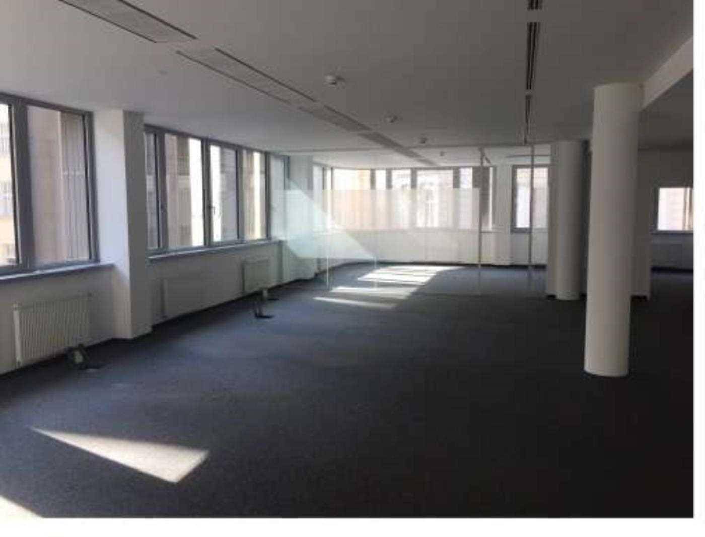 Geräumiger, leerer Großraumbüro mit Säulen, Heizkörpern und großen Fensterfronten für viel Tageslicht.