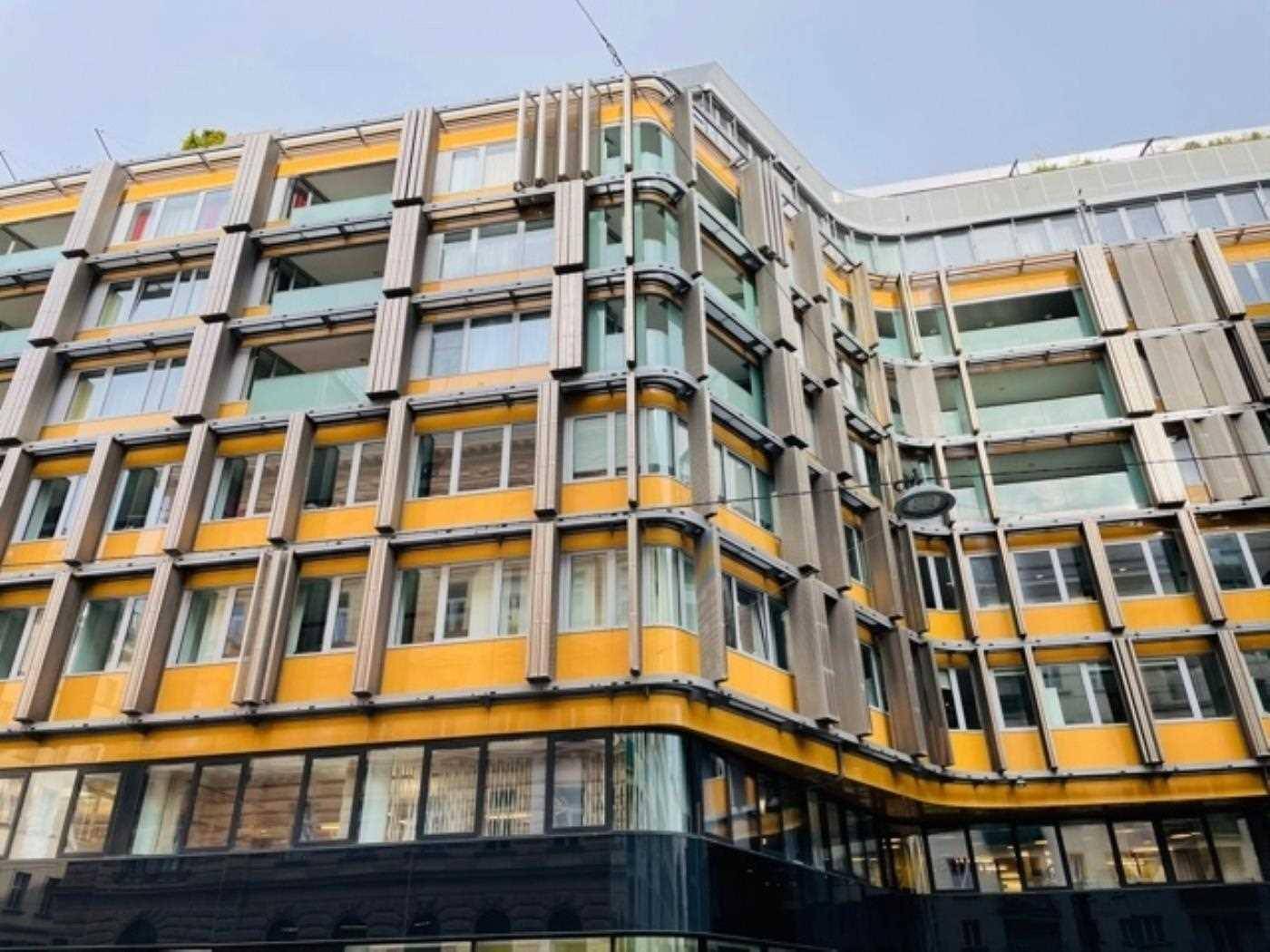 Detailansicht der modernen Gebäudefassade mit gelben und grauen Paneelen sowie großen Fensterflächen.