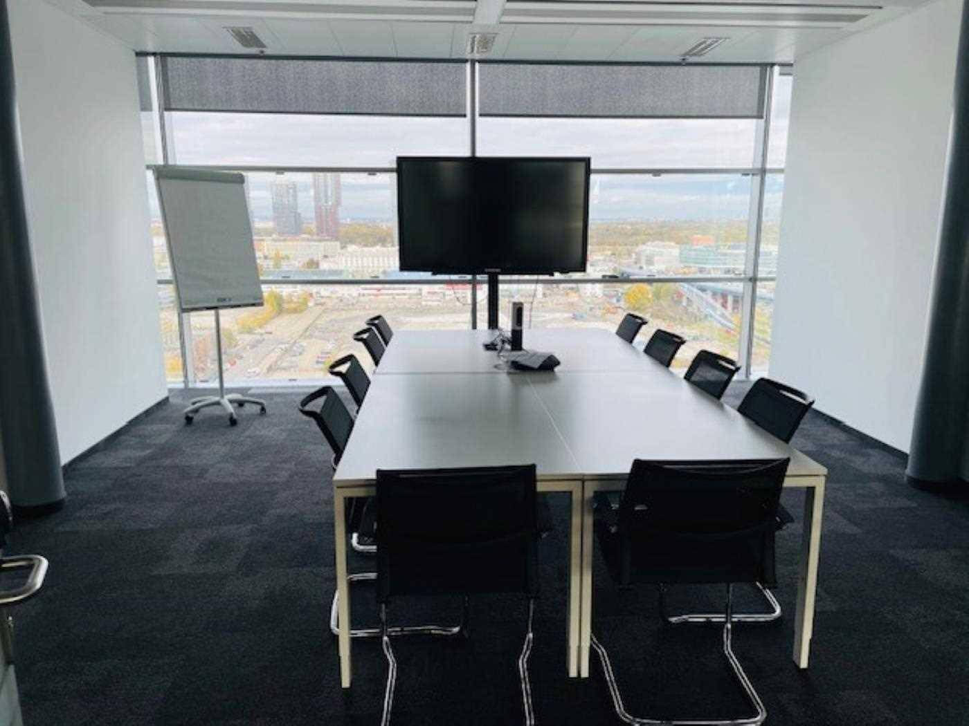 Geräumiger Konferenzraum mit großem Tisch, TV-Bildschirm und weitem Stadtblick durch Panoramafenster.