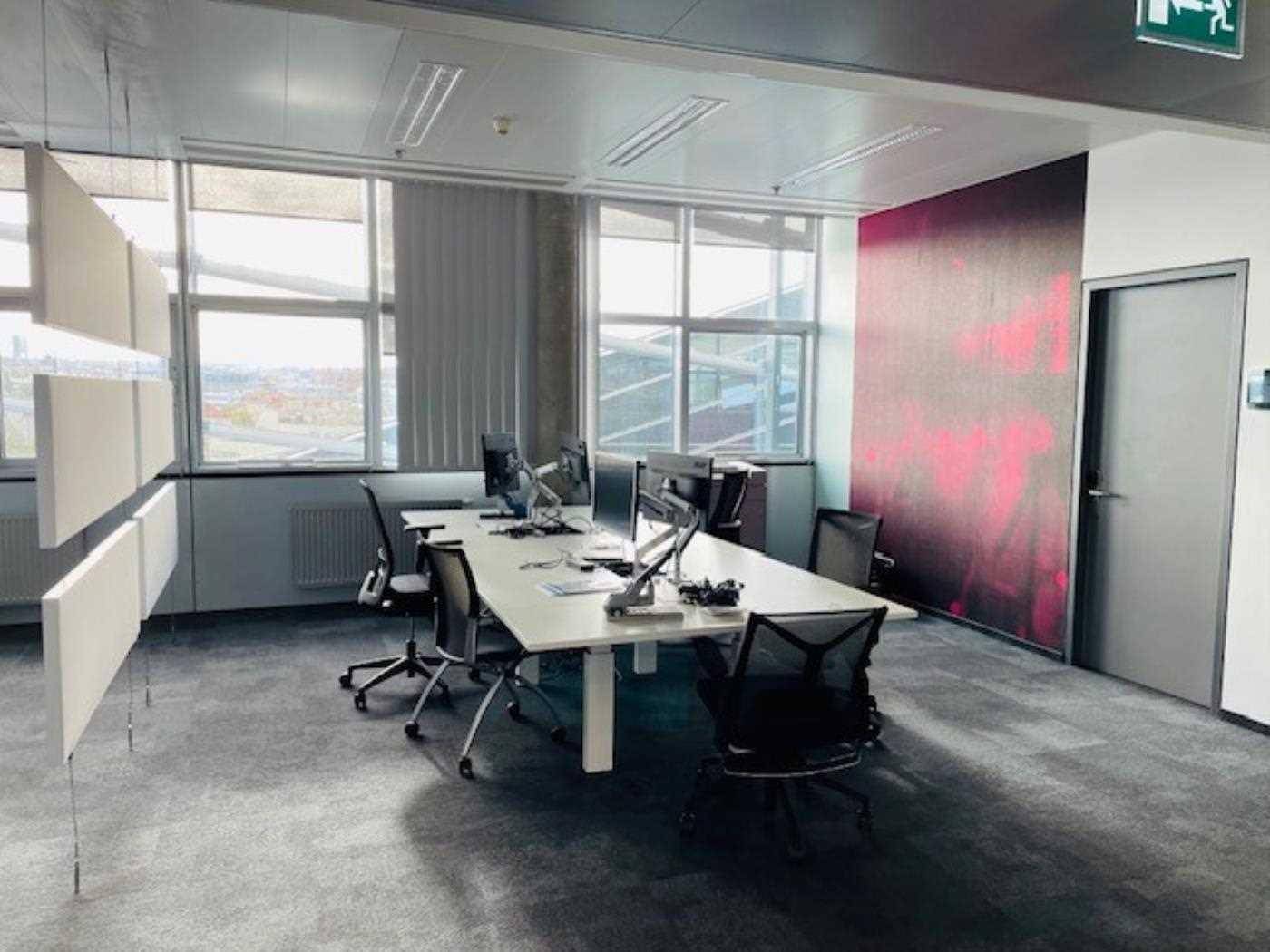 Büroraum mit mehreren Arbeitsplätzen, Computern und einer auffälligen pinken Akzentwand.