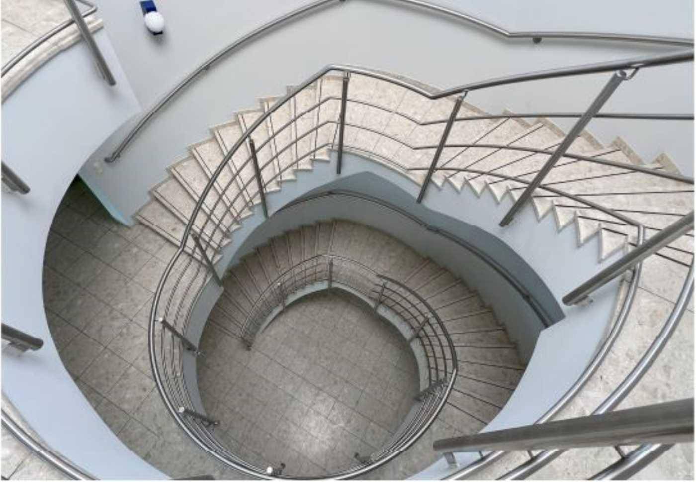 Blick von oben auf eine elegante Wendeltreppe mit Metallgeländer und Fliesenstufen.