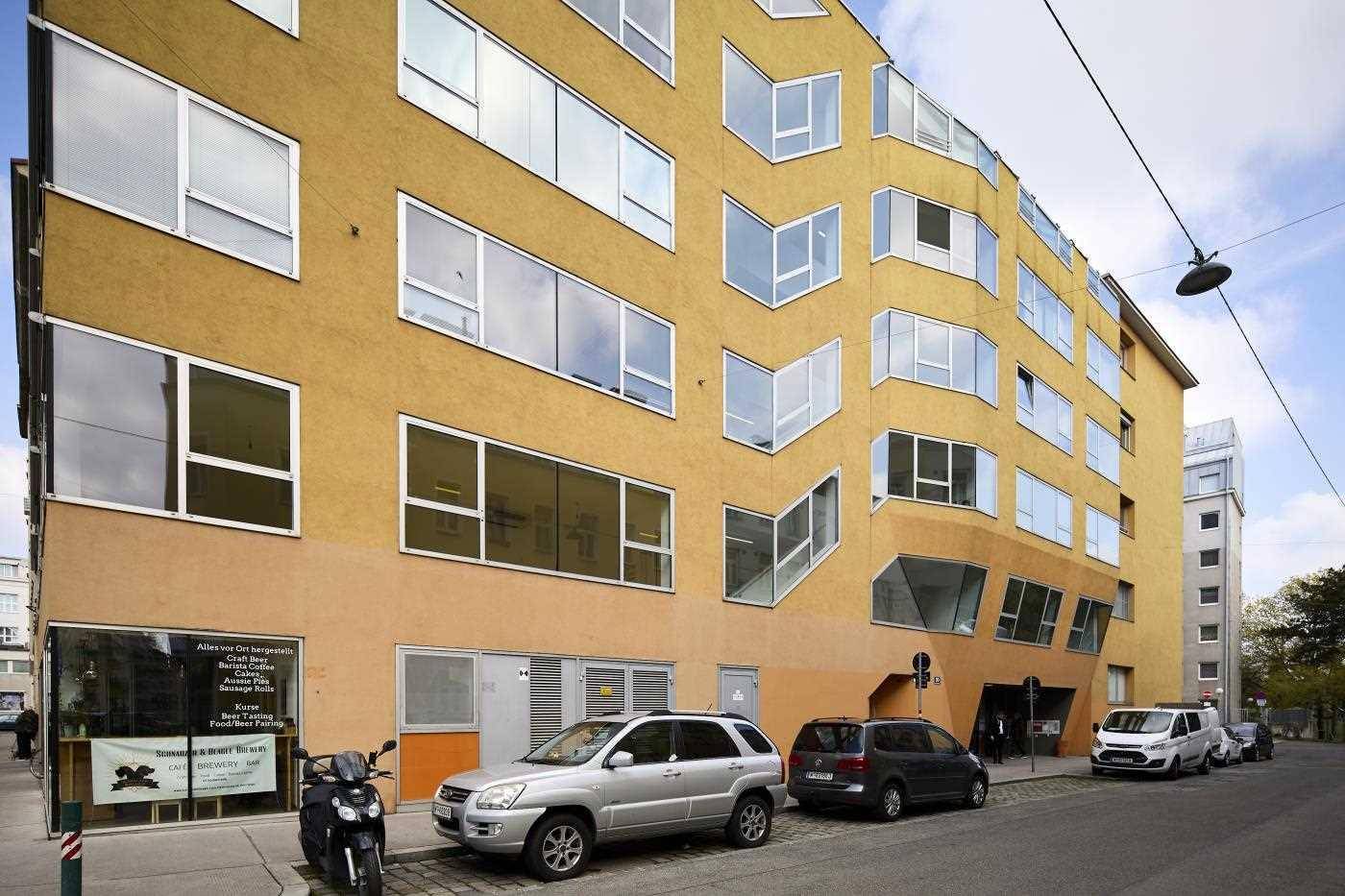 Gebäude mit auffälliger gelber Fassade und vielen unregelmäßig geformten Fenstern entlang einer Straße.