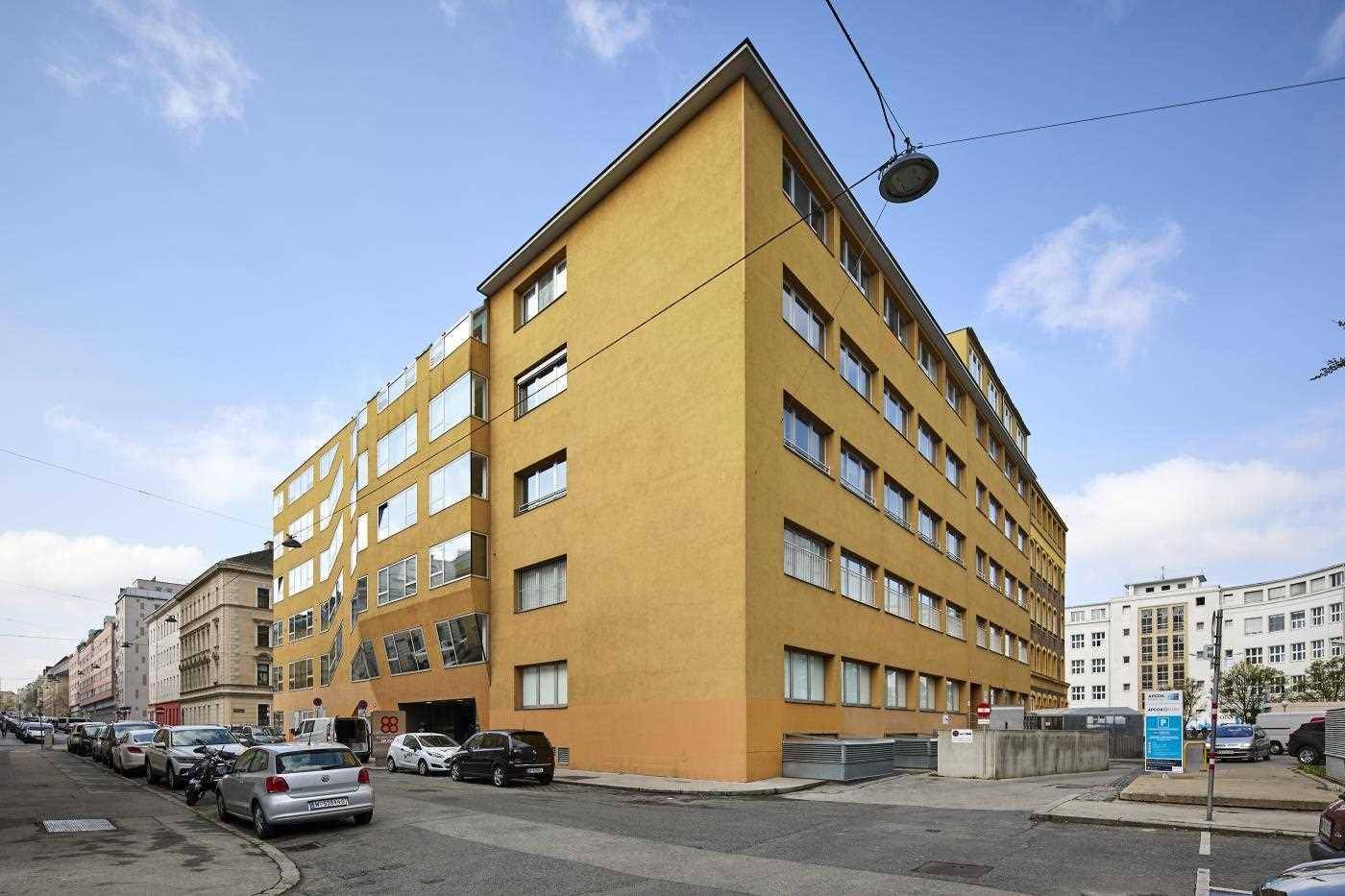 Langes, gelbes Bürogebäude mit vielen Fenstern und einer modernen Architektur entlang einer belebten Straße.