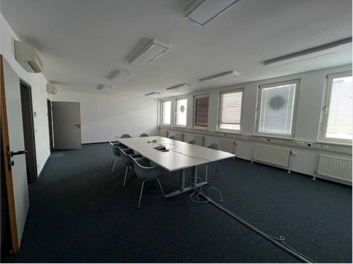 Geräumiger Konferenzraum mit großem Tisch, Stühlen, Fenstern und Klimaanlagen.