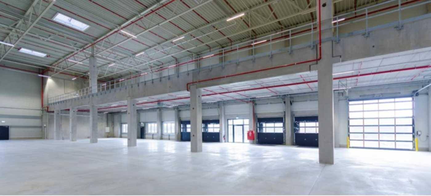 Große Lagerhalle mit mehreren Rolltoren für LKW-Zugang, Betonboden und einer erhöhten Mezzanine-Ebene.