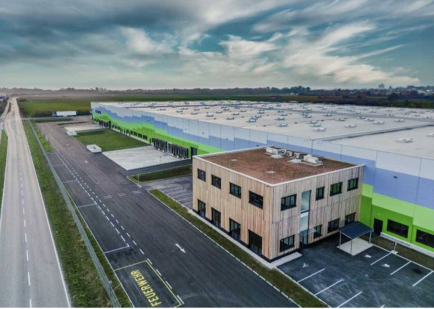 Nahaufnahme des modernen Bürogebäudes mit Holzfassade, angrenzend an das große Logistikzentrum.