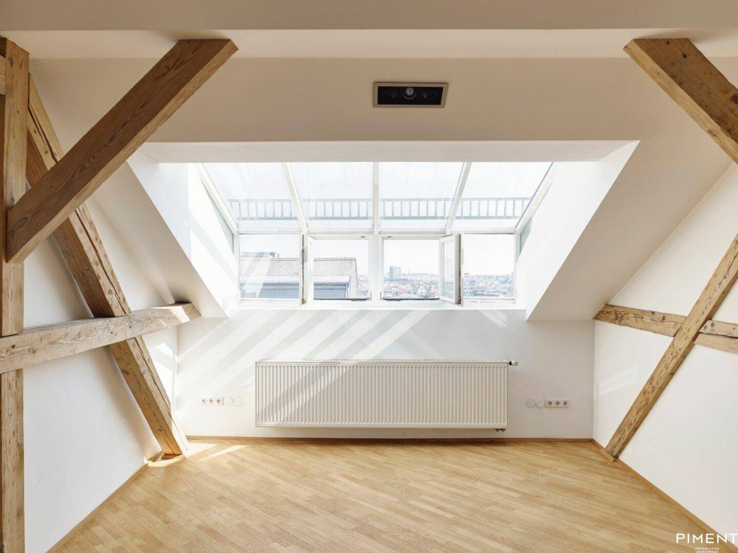 Heller Dachbodenraum mit großen Dachfenstern, Heizkörper und sichtbaren Holzbalken.