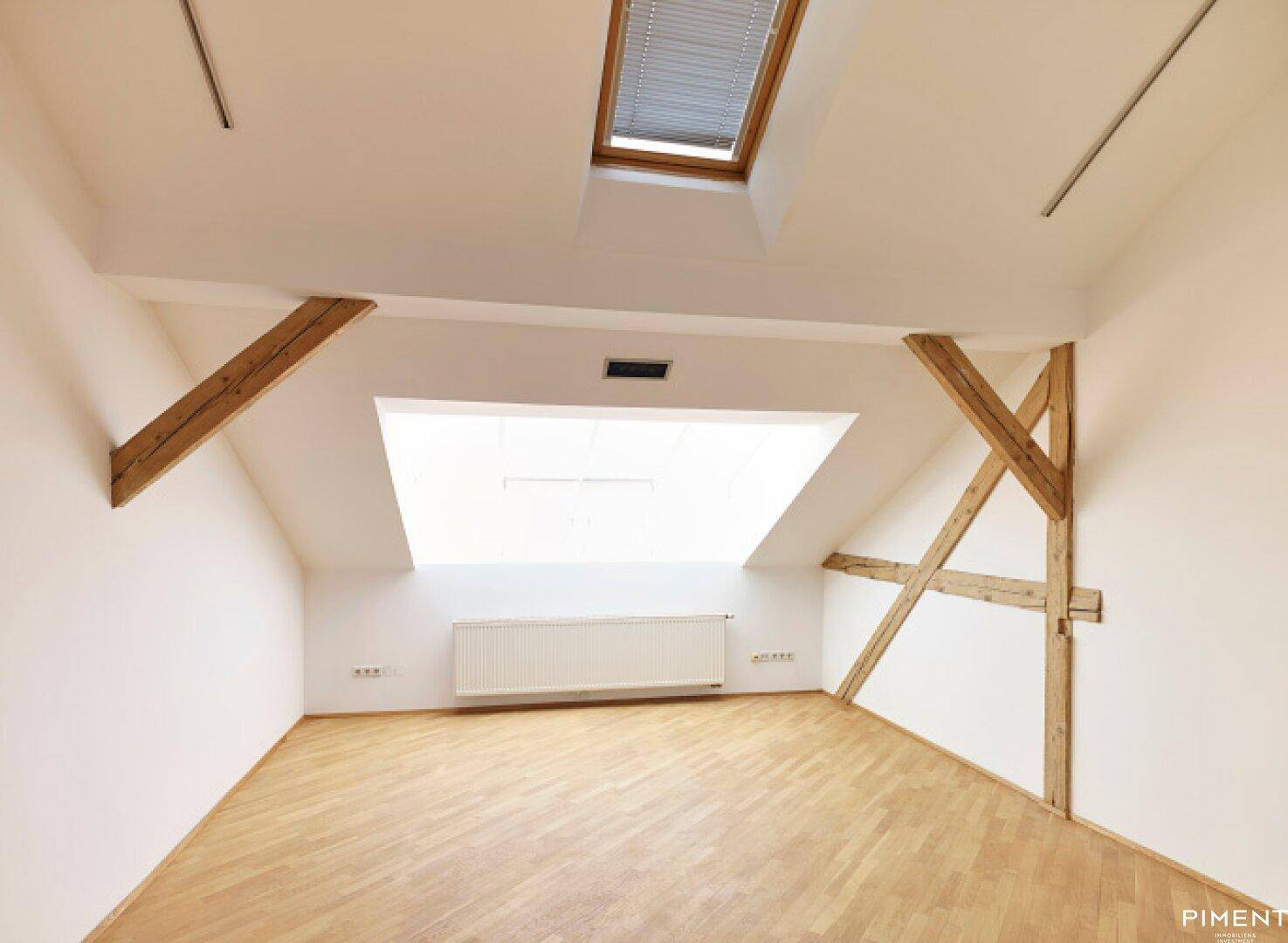 Dachbodenraum mit Holzbalken, Dachfenster und hellem Parkettboden.