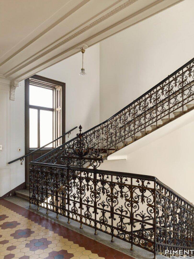 Historisches Treppenhaus mit kunstvollem schmiedeeisernem Geländer und gemusterten Fliesen.