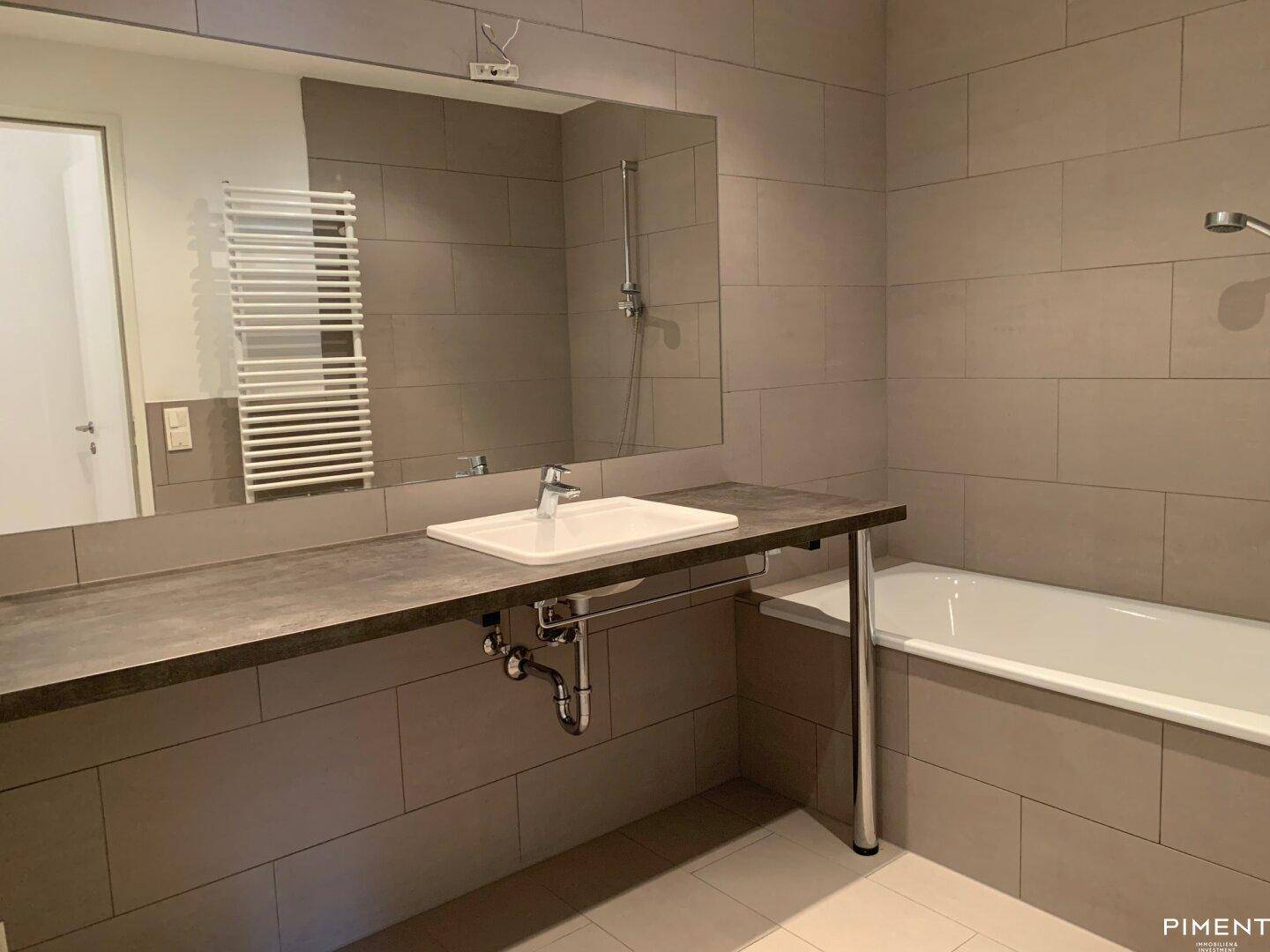 Modernes Badezimmer mit Badewanne, großem Spiegel und beheiztem Handtuchhalter an der Wand.