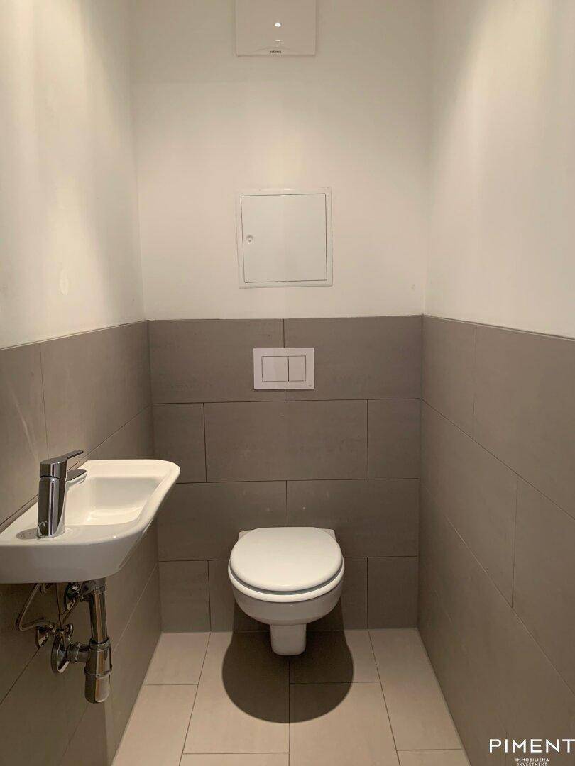 Modernes Gäste-WC mit Wand-WC, kleinem Waschbecken und grauen Fliesen an den Wänden.