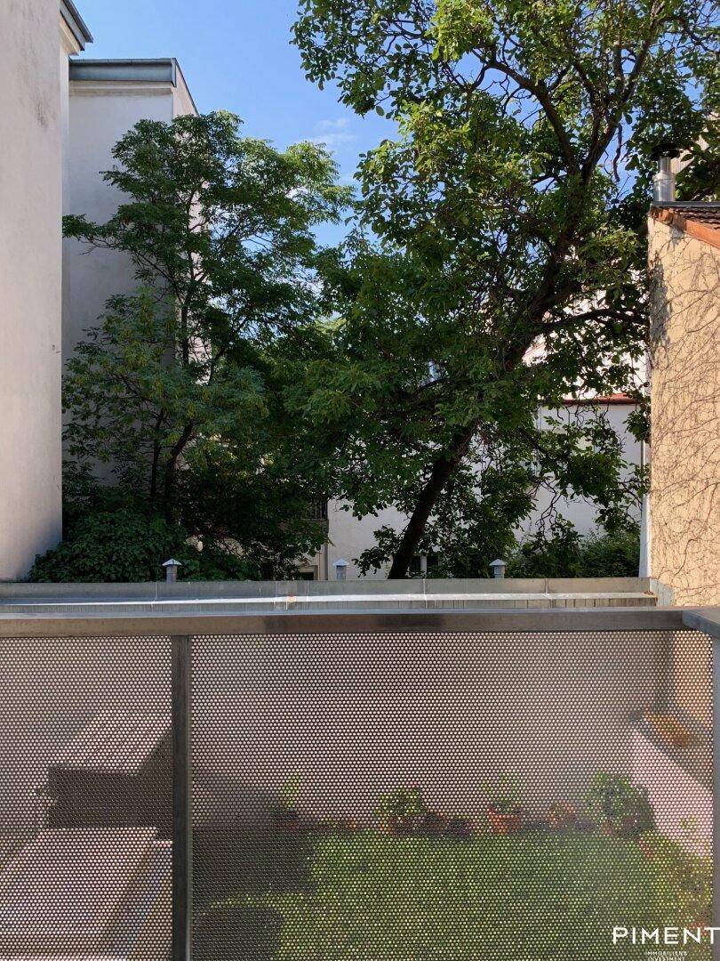 Kleiner, gepflegter Gartenbereich mit Bäumen und einer modernen Metallabtrennung im Innenhof.