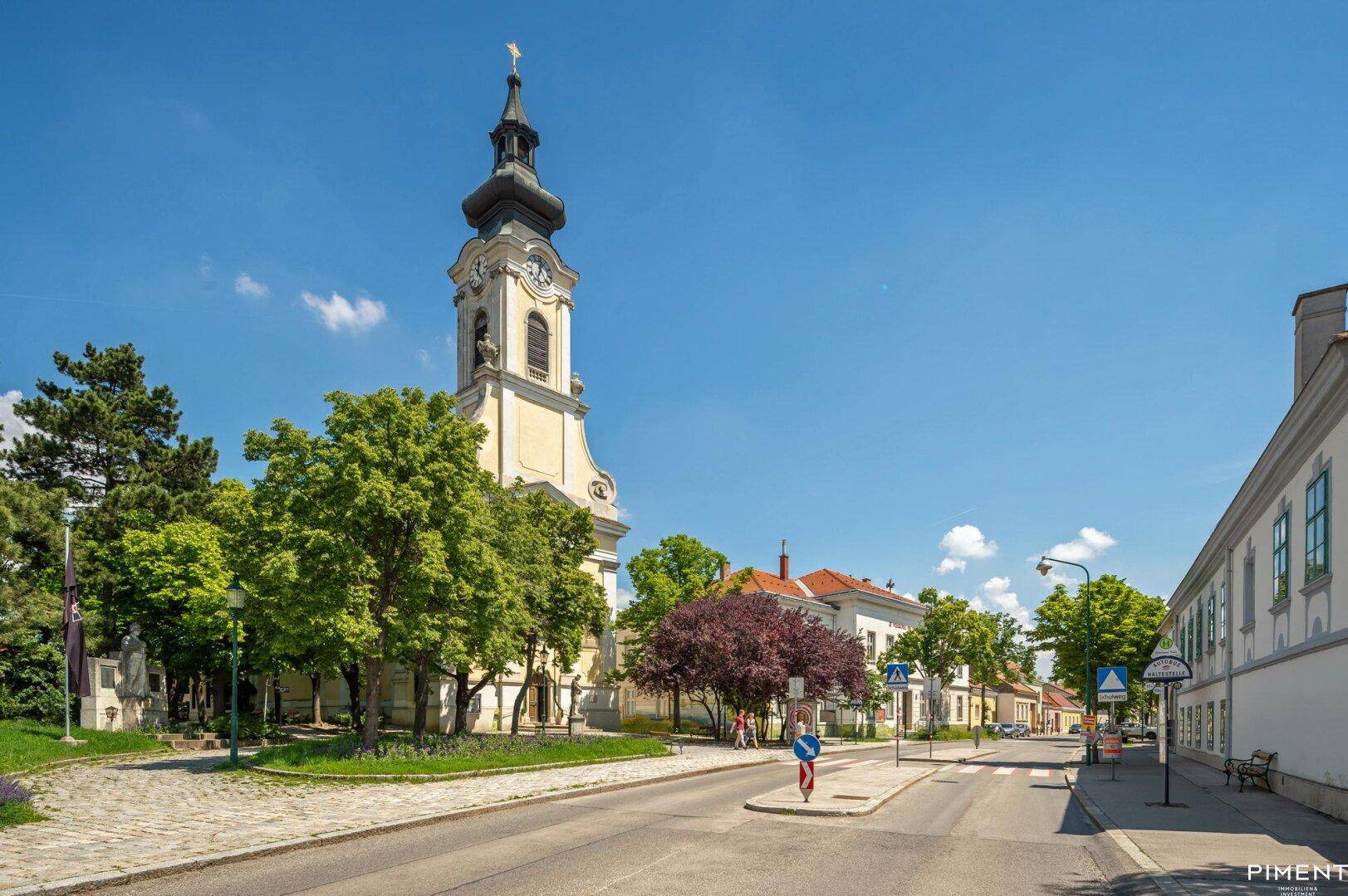 Historische Kirche und traditionelle Gebäude entlang einer Straße unter blauem Himmel.