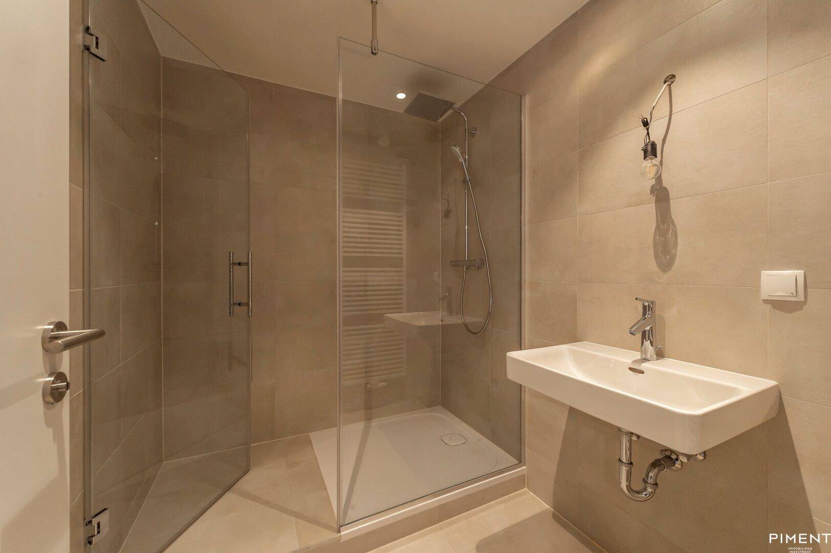 Modernes Badezimmer mit begehbarer Dusche, Einzelwaschbecken und hellen Fliesen.