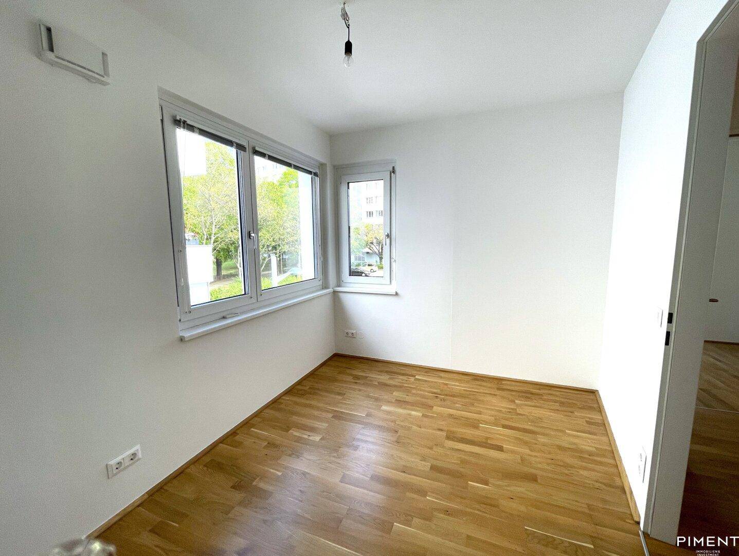 Helles Schlafzimmer mit Parkettboden und Fenstern, die einen Blick ins Grüne bieten.