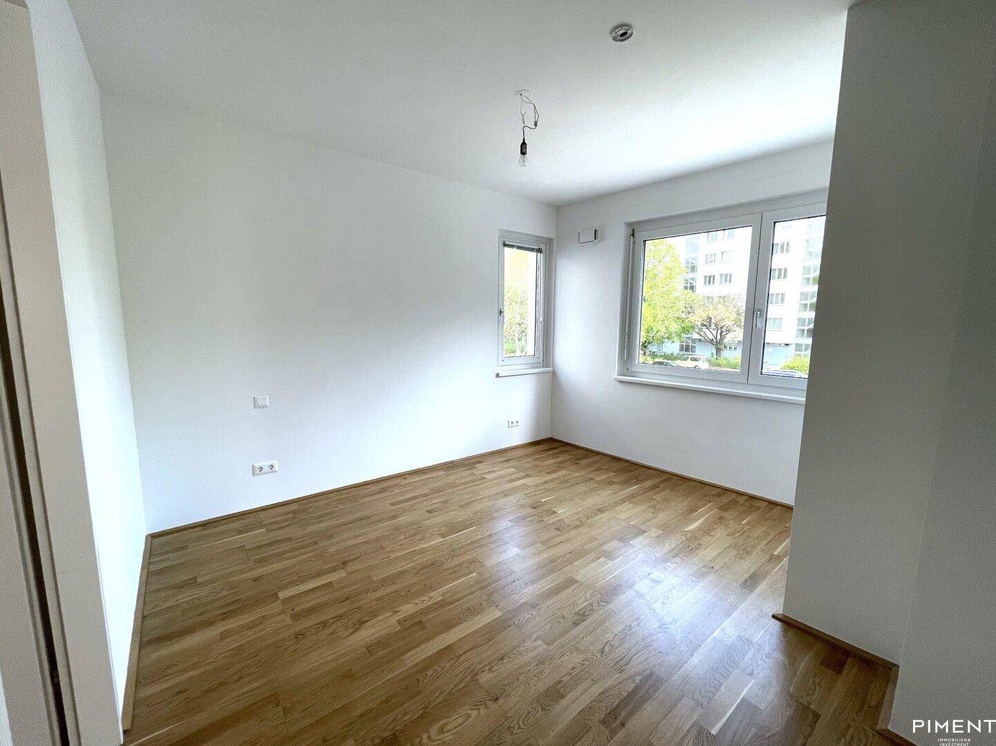 Geräumiges Zimmer mit Parkettboden und großen Fenstern, die viel Tageslicht hereinlassen.