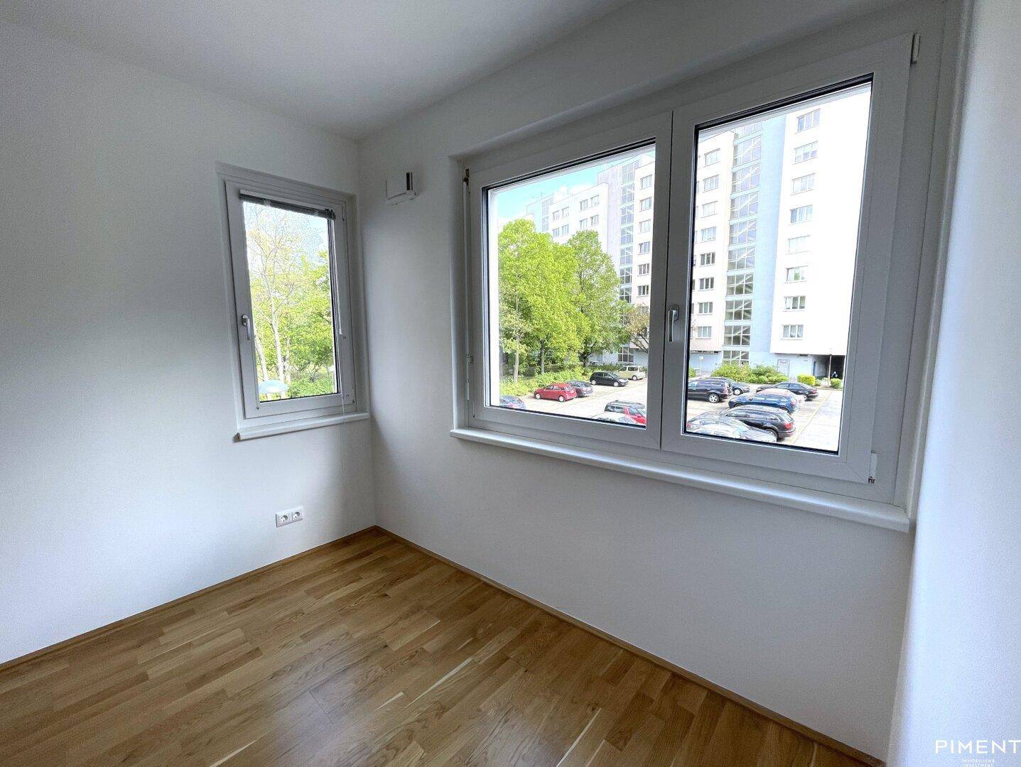 Helles Zimmer mit Parkettboden und Blick auf die umliegende Bebauung und Grünflächen.
