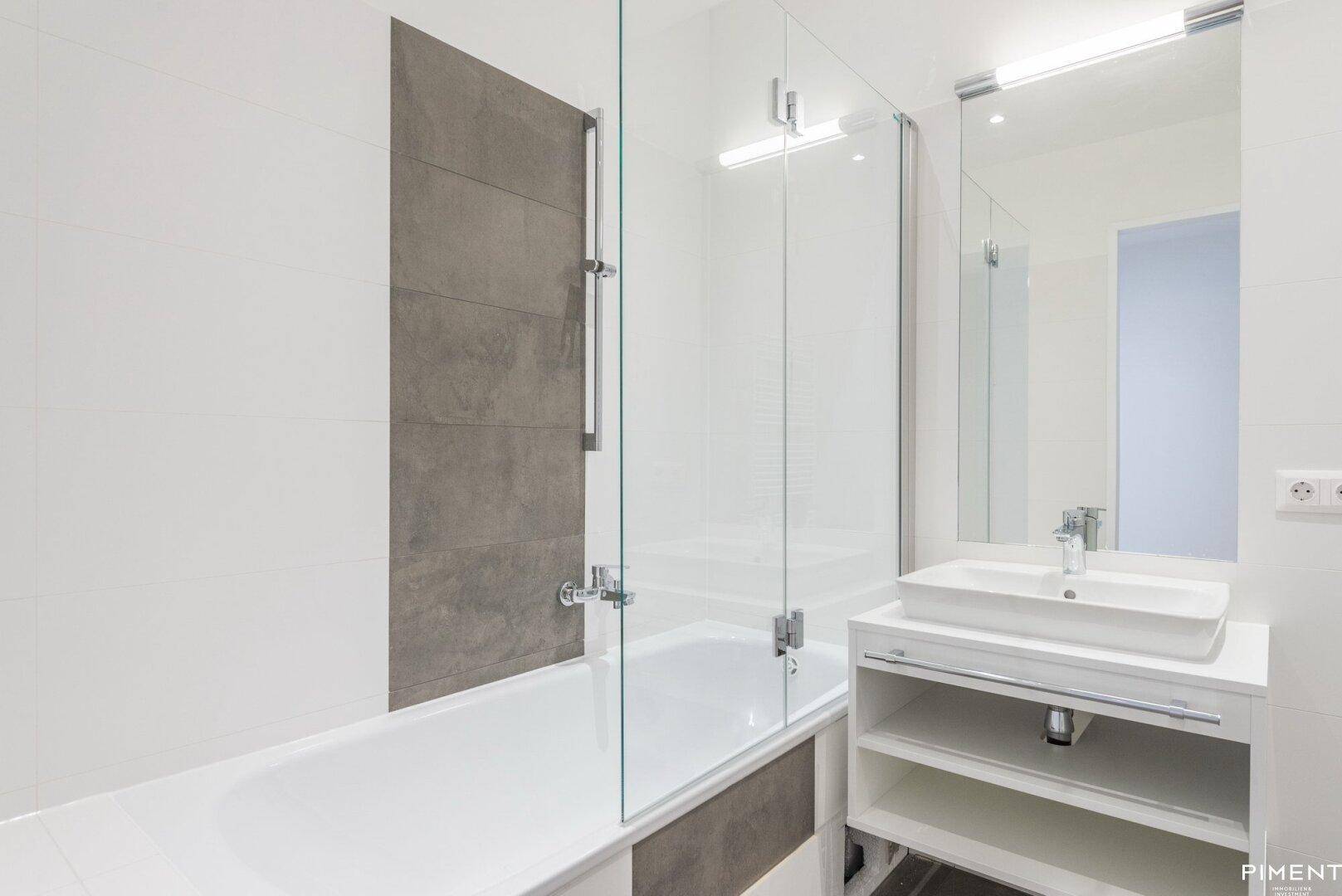 Modernes Badezimmer mit Badewanne, Glasabtrennung und eleganten grauen Fliesen.