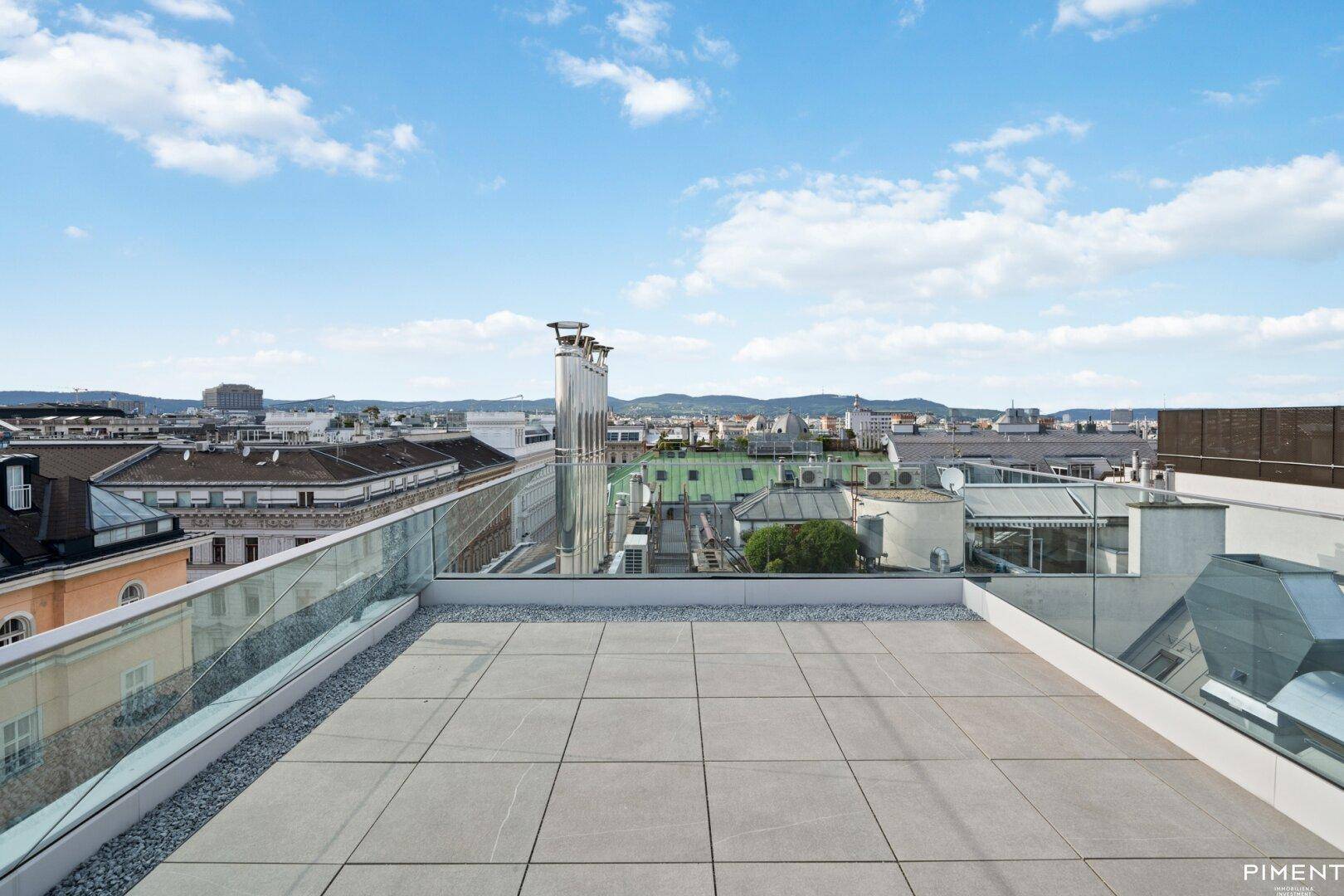 Weitläufige Dachterrasse mit Stadtblick und Glasgeländer.