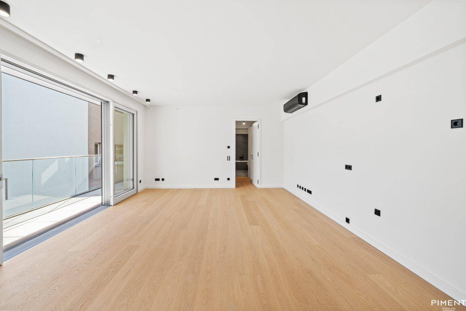 Geräumiger, heller Wohnbereich mit Parkettboden, Klimaanlage und Zugang zu einem Balkon.