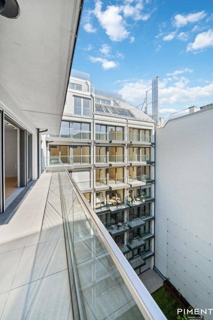 Langer Balkon mit Glasgeländer und Blick auf die moderne Gebäudefassade und den Innenhof.