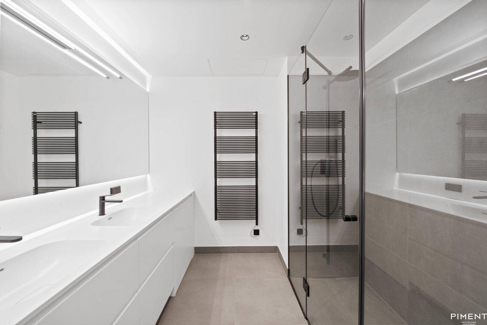 Modernes Badezimmer mit Doppelwaschbecken, begehbarer Dusche und beheiztem Handtuchhalter.