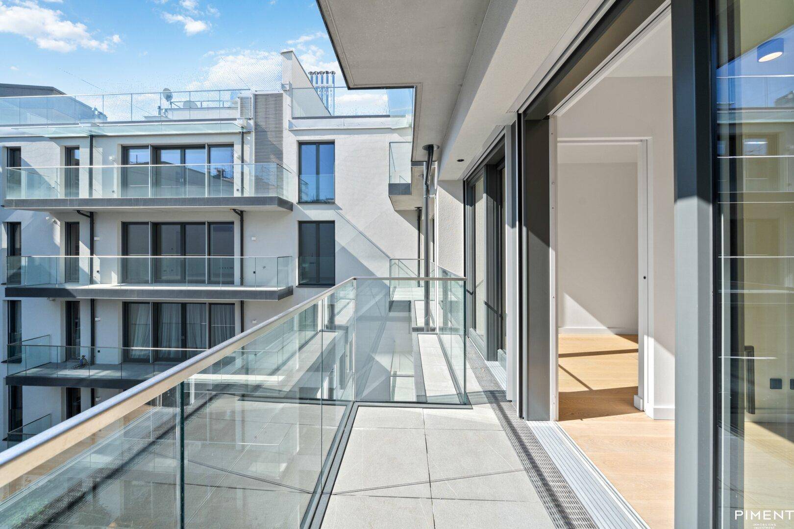 Geräumiger Balkon mit Glasgeländer und Blick auf die moderne Wohnanlage.