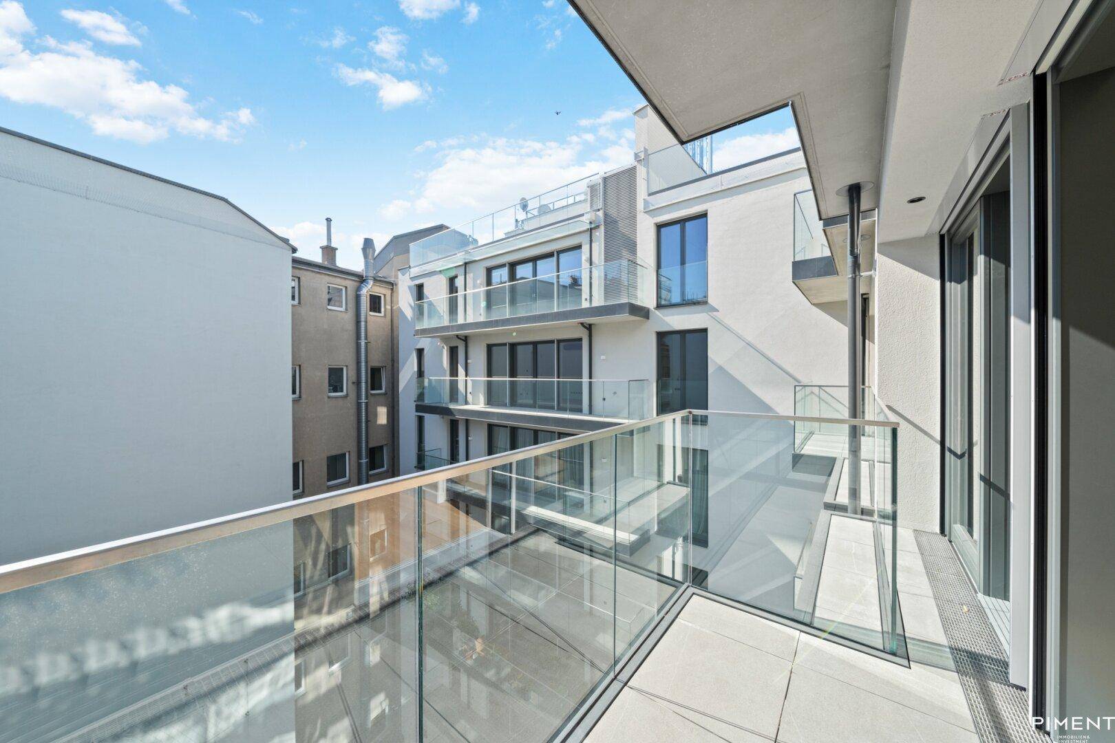 Heller Balkon mit Glasbrüstung und Aussicht auf den Innenhof und umliegende Gebäude.