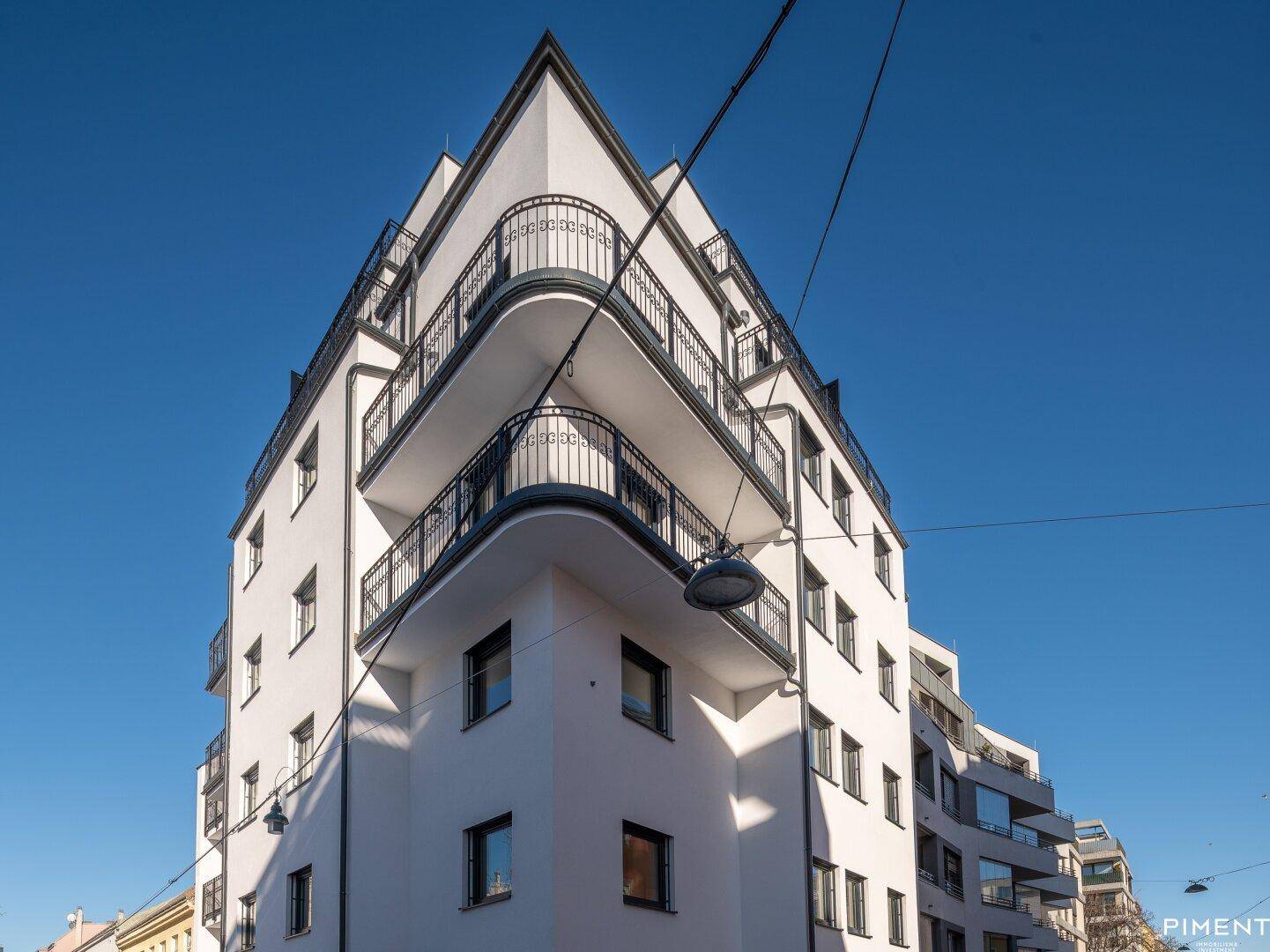 Modernes Eckgebäude mit weißer Fassade und geschwungenen Balkonen unter strahlend blauem Himmel.