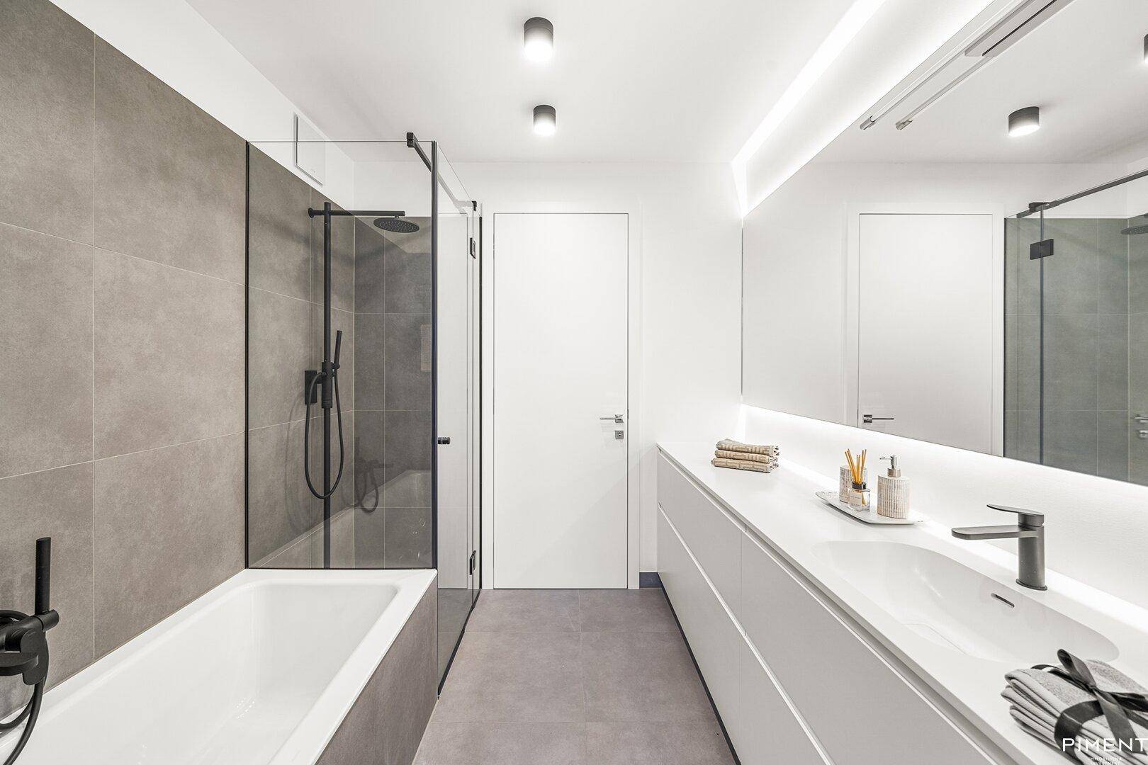 Modernes Badezimmer mit Badewanne, separater Dusche und großem Spiegel mit Beleuchtung.