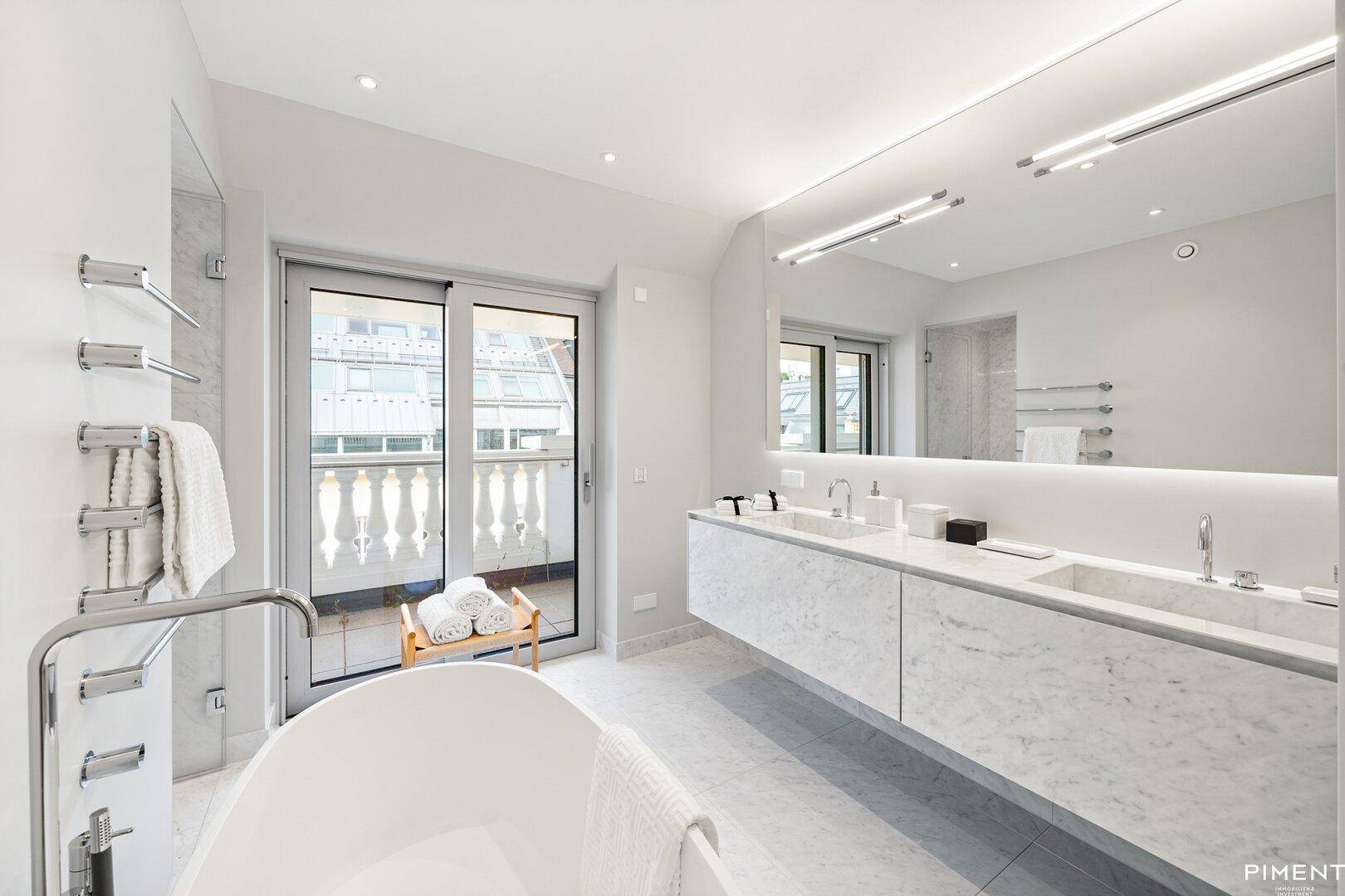 Luxuriöses Badezimmer mit freistehender Badewanne, Doppelwaschbecken und Balkonzugang.