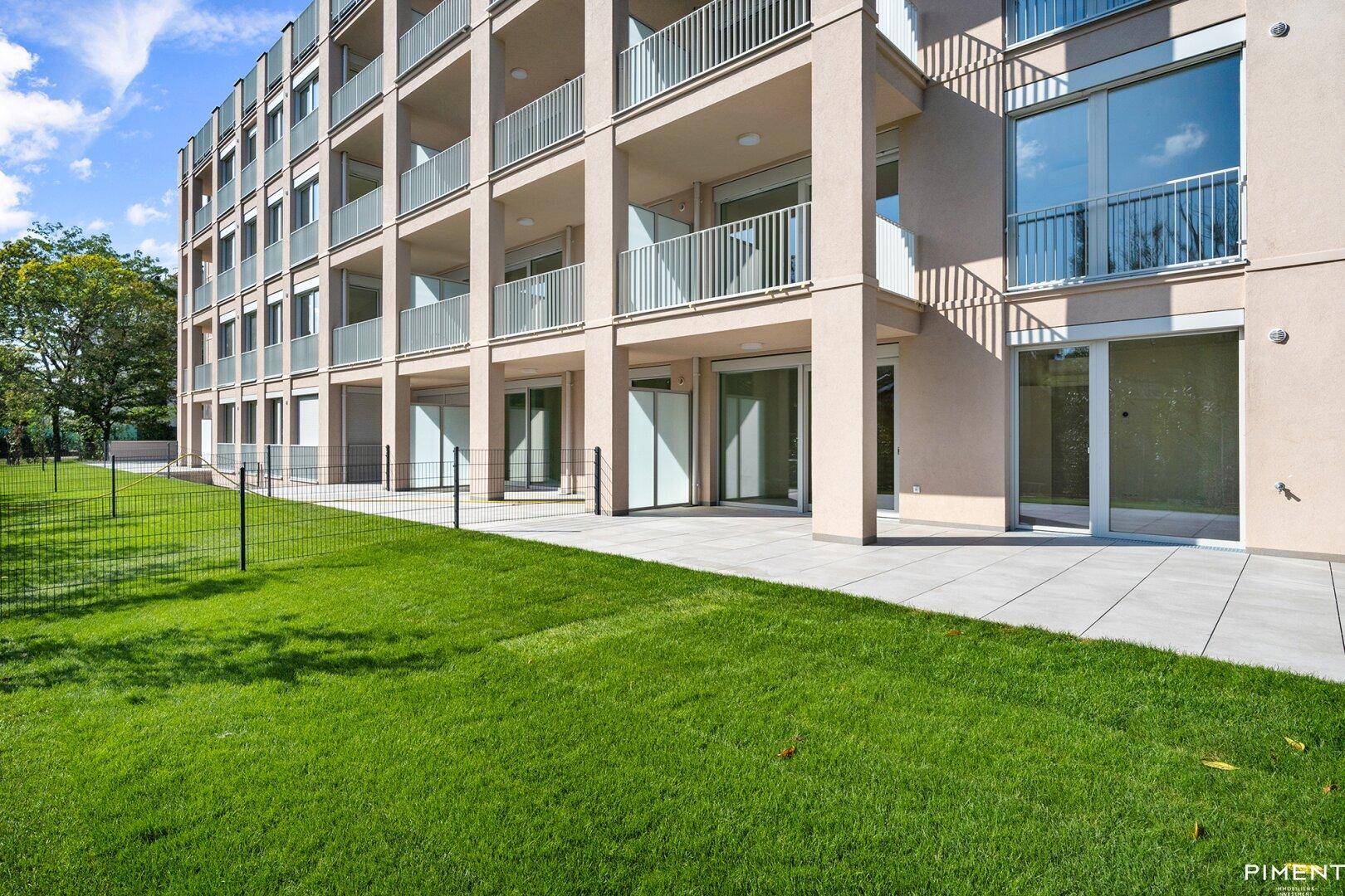 Gepflegte Rasenfläche und eine gepflasterte Terrasse im Erdgeschoss eines modernen Wohngebäudes.