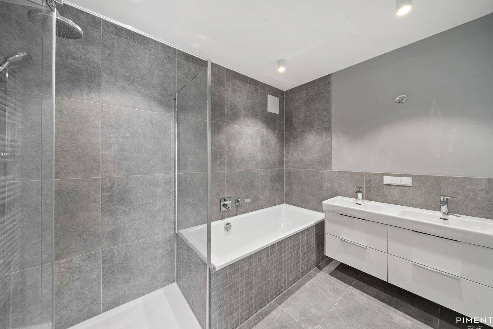 Modernes Badezimmer mit grauen Fliesen, Doppelwaschbecken, Badewanne und Dusche.