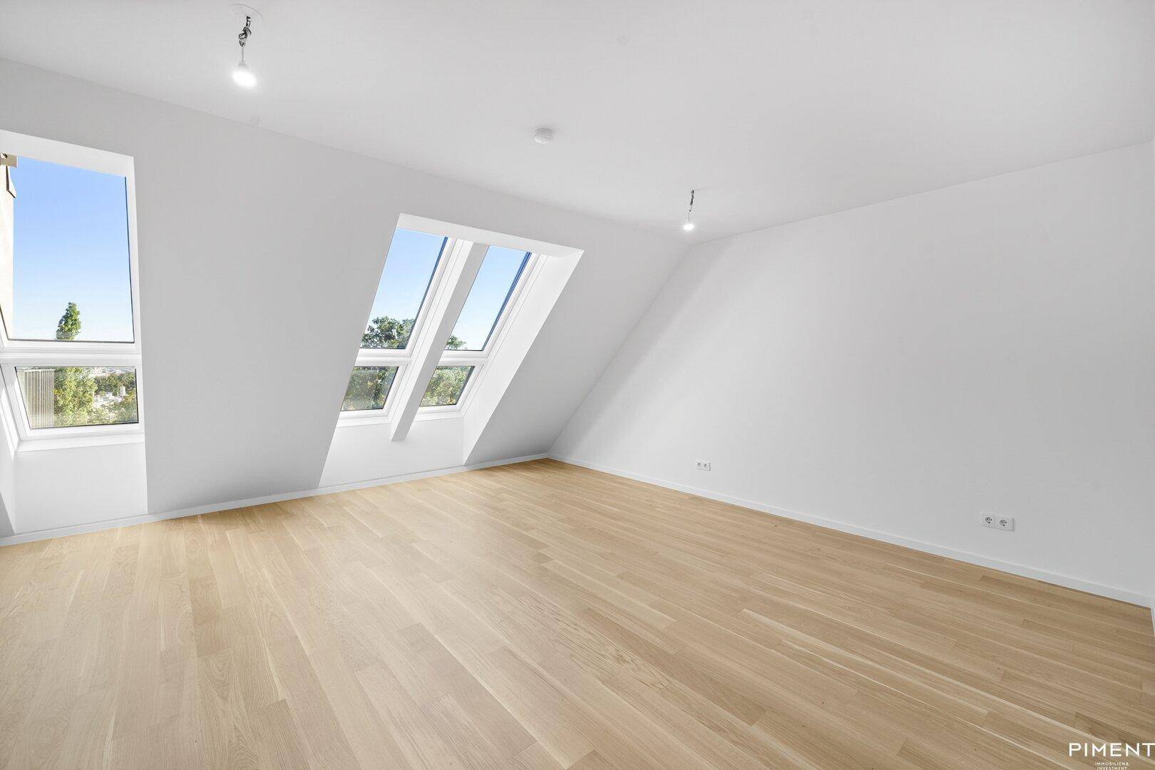 Geräumiger Dachgeschossraum mit Holzboden, weißen Wänden und mehreren Dachfenstern.