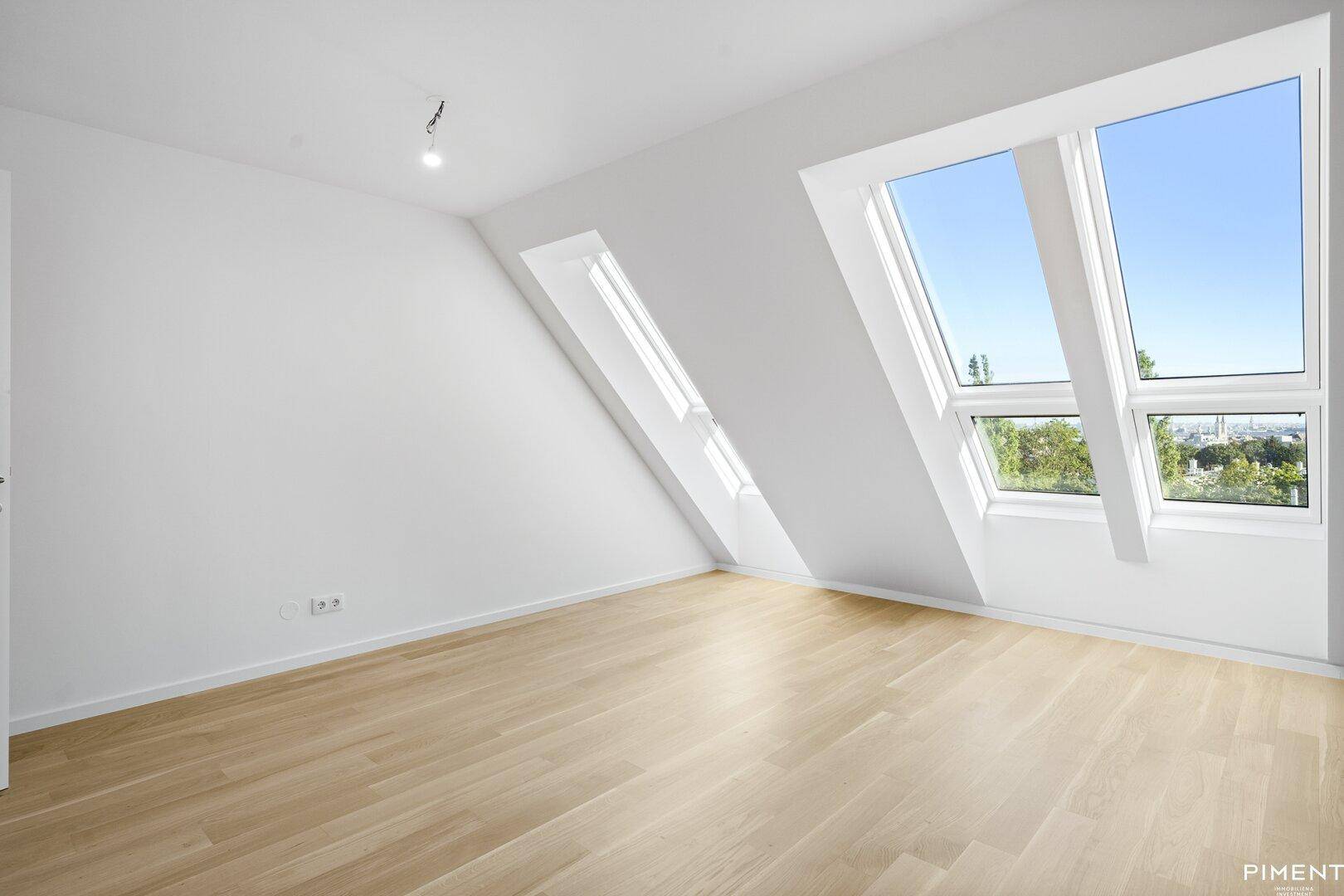 Heller Dachgeschossraum mit schrägen Wänden, Holzboden und großen Dachfenstern.