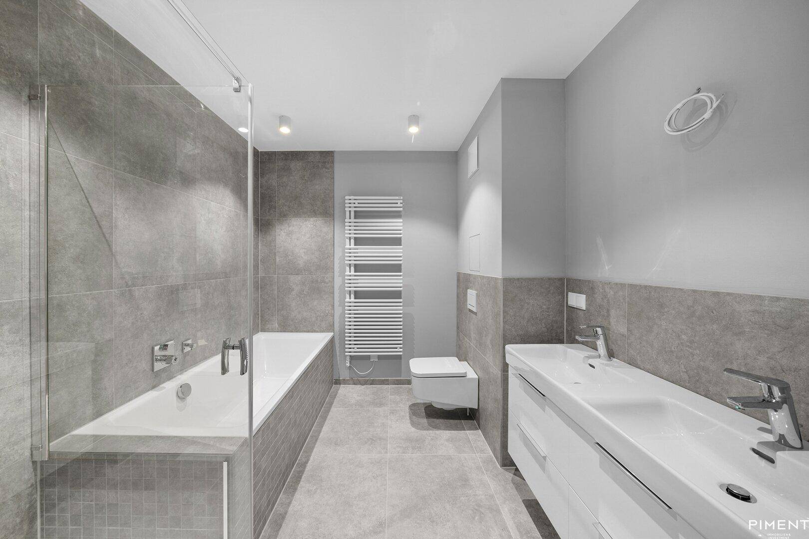 Modernes Badezimmer mit Doppelwaschbecken, Badewanne und grauen Fliesen.