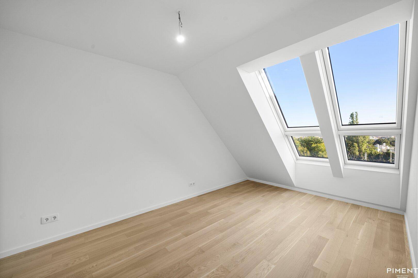Dachzimmer mit Holzboden, weißen Wänden und großen Dachfenstern für viel Tageslicht.