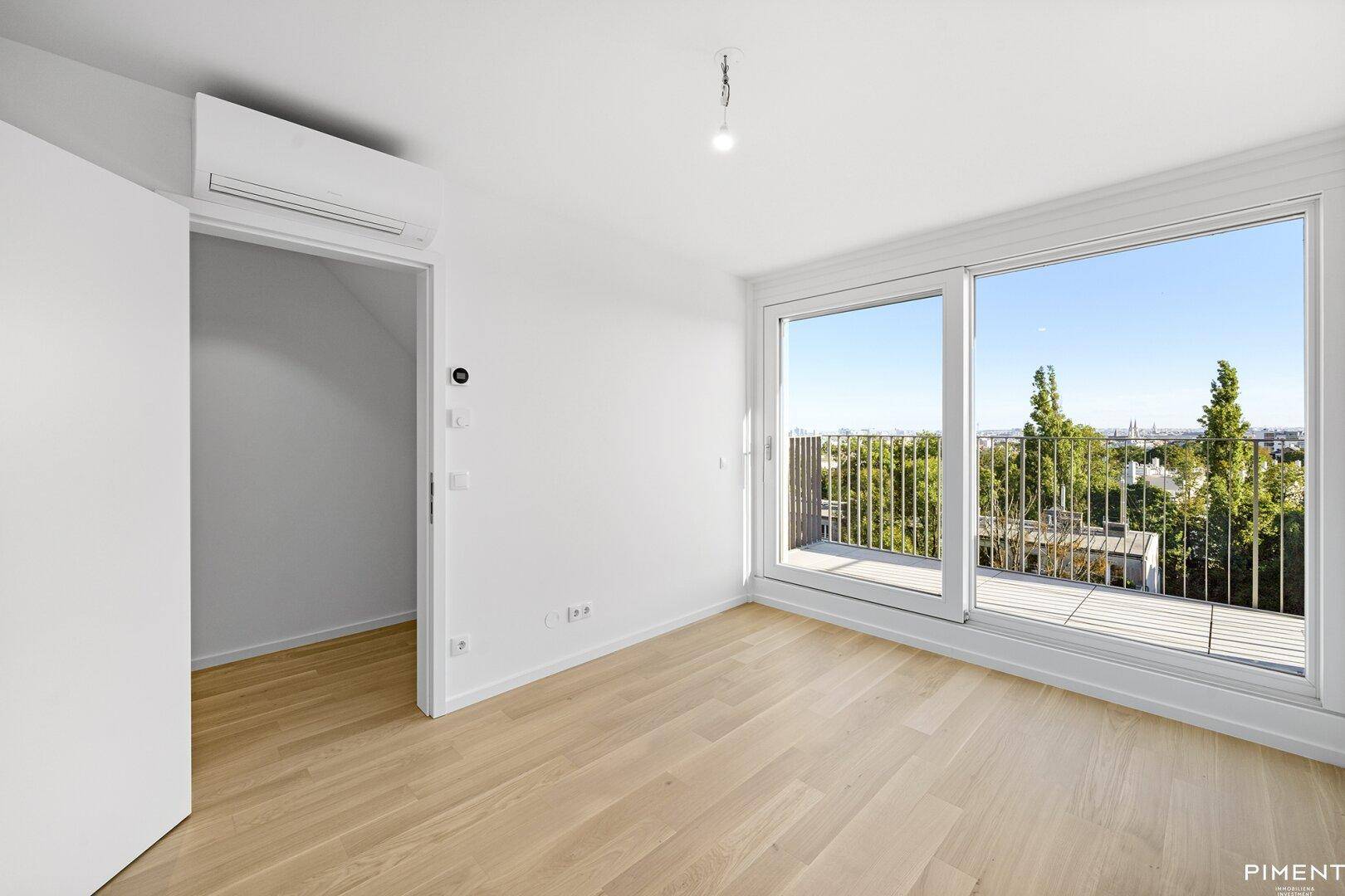 Helles Schlafzimmer mit Holzboden, Klimaanlage und Zugang zu einem Balkon.