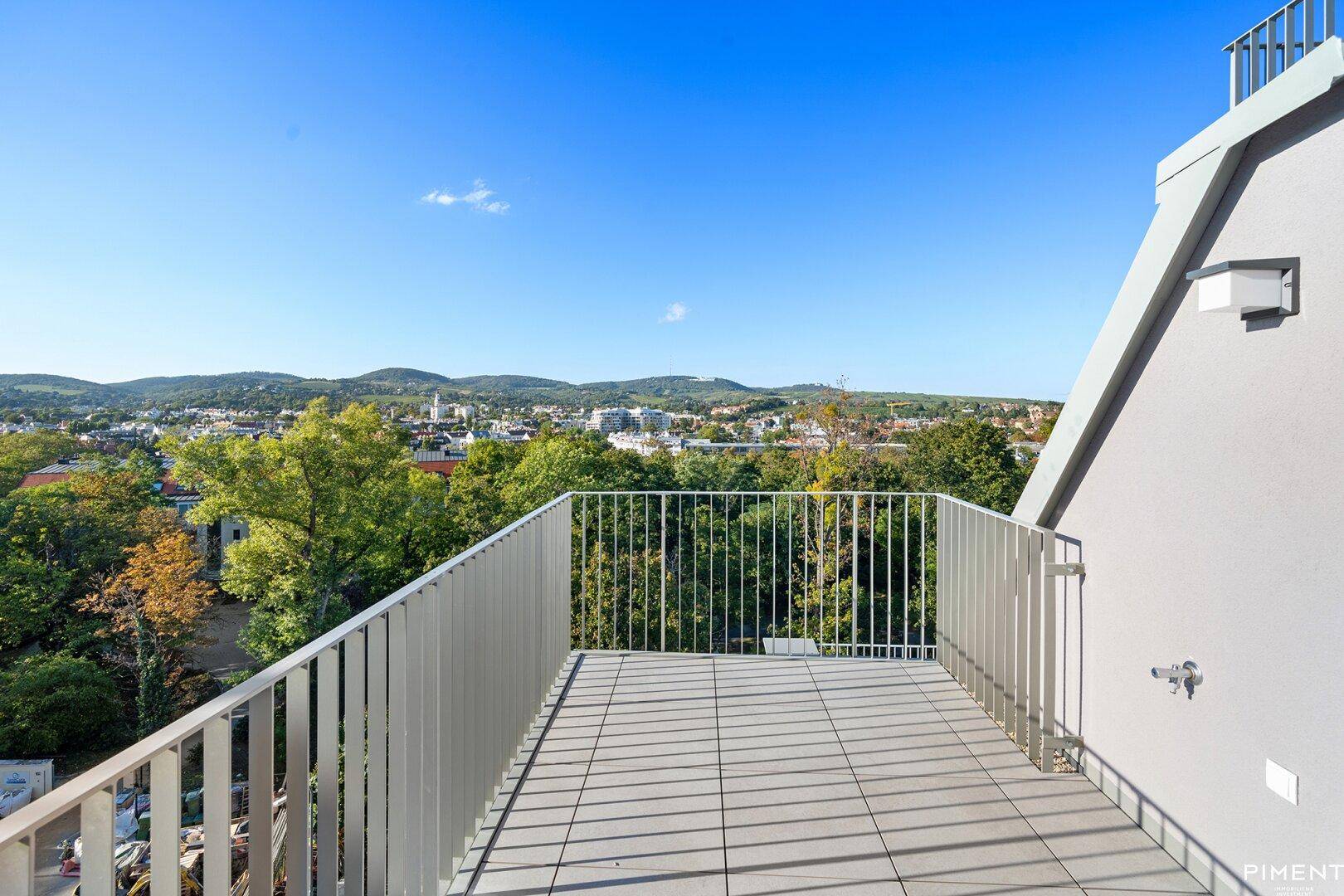 Große Dachterrasse mit Fliesenboden und weitem Blick über die Stadt und grüne Hügel.