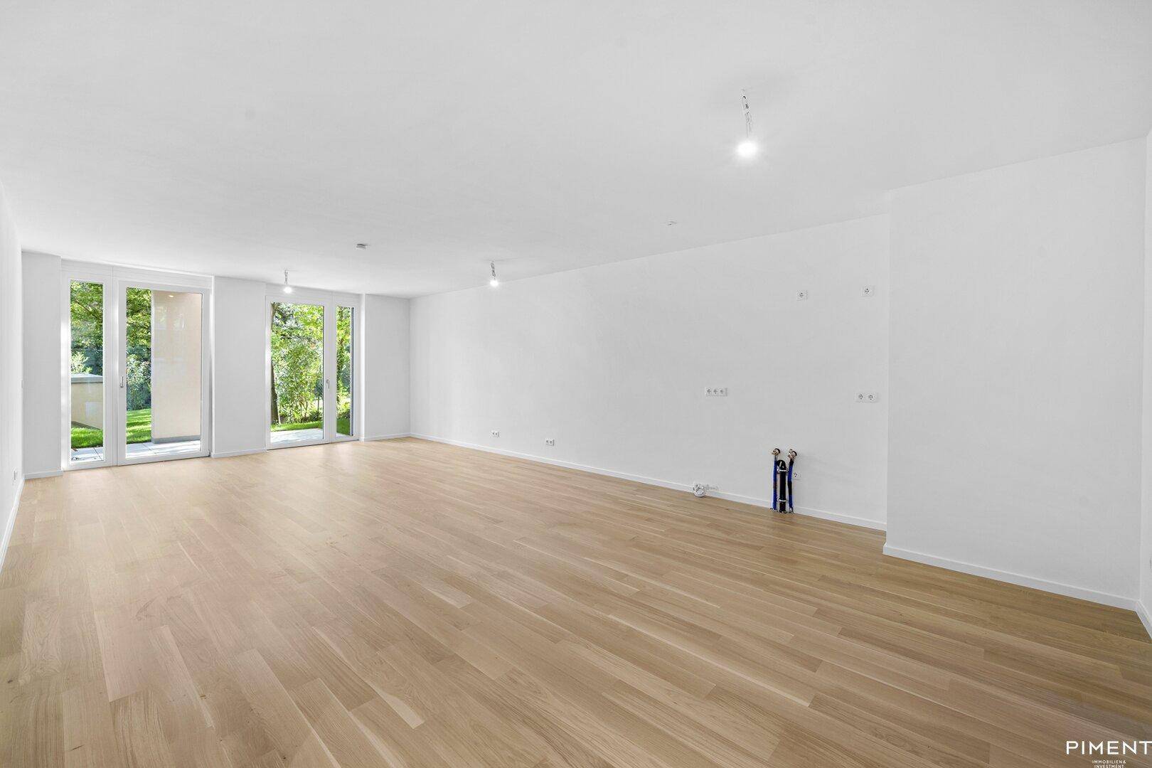 Geräumiges, leeres Wohnzimmer mit hellem Parkettboden und großen Fenstern zum Garten.