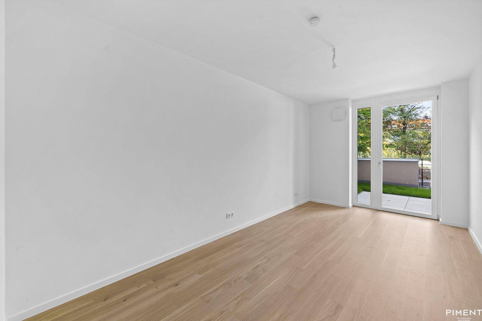 Heller Raum mit Parkettboden und einer Fenstertür, die den Blick ins Grüne freigibt.