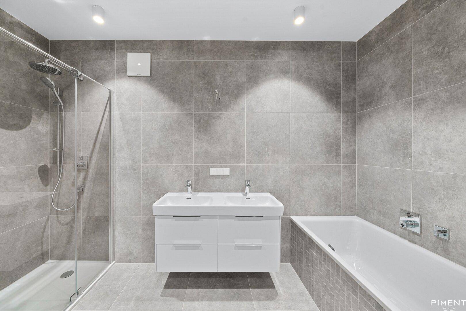 Modernes Badezimmer mit grauen Fliesen, Doppelwaschbecken, Dusche und Badewanne.
