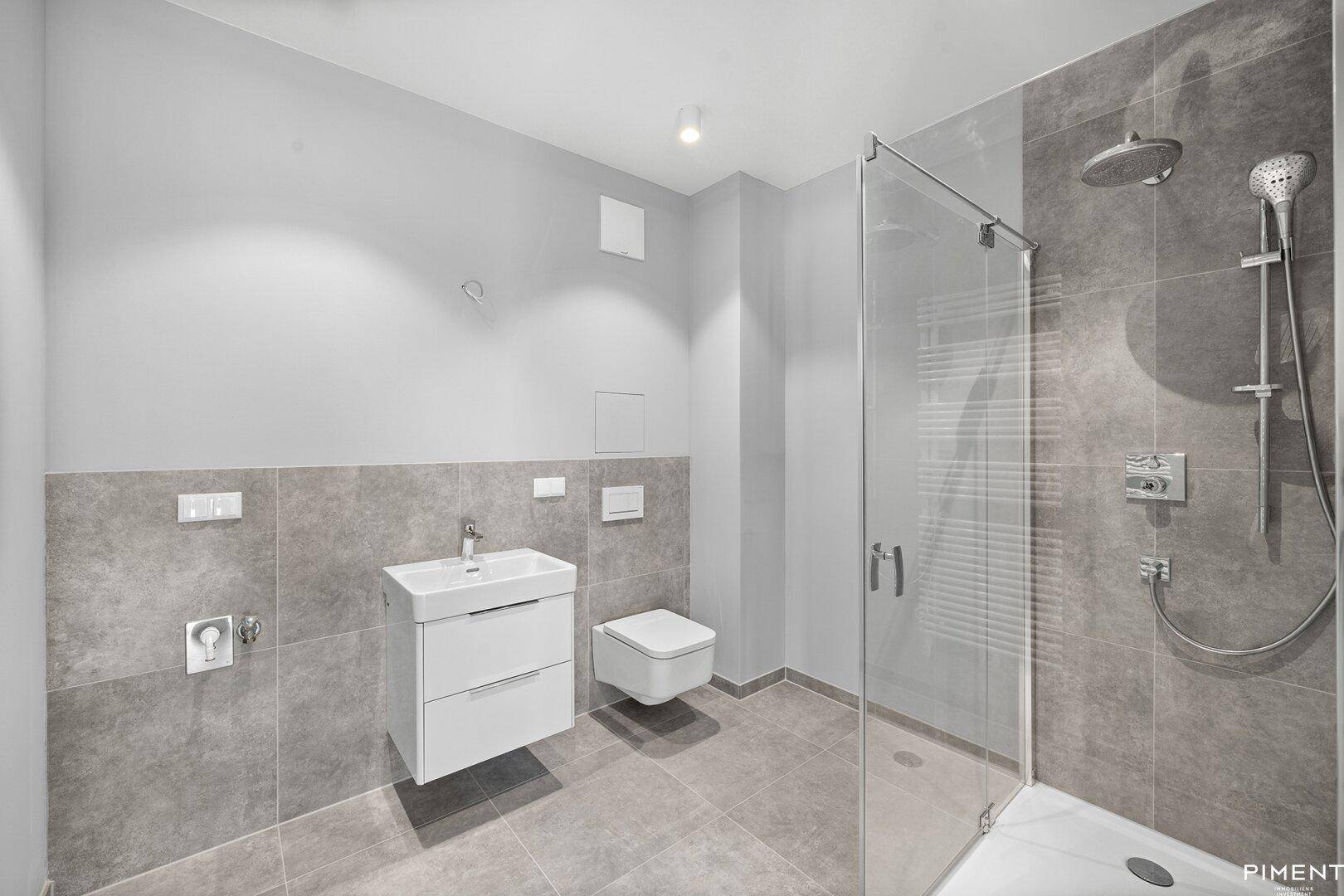 Modernes Badezimmer mit grauen Fliesen, einer ebenerdigen Dusche und einem wandhängenden WC.