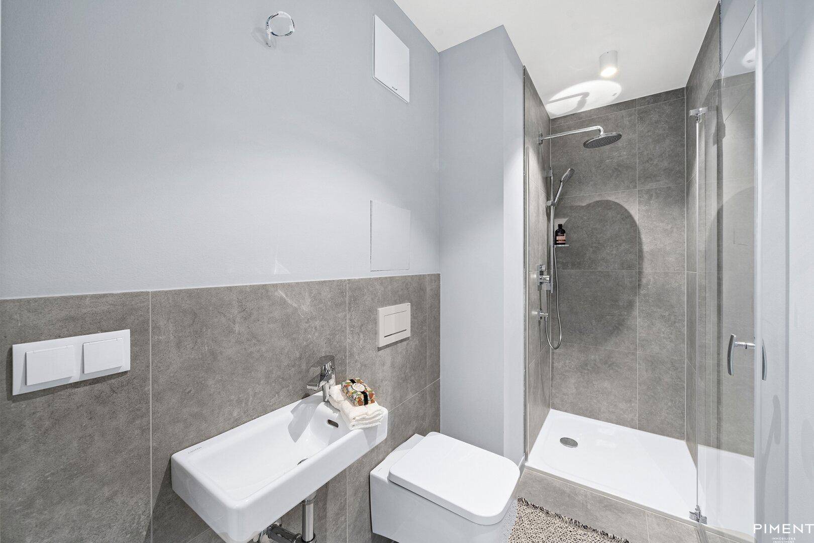 Modernes Badezimmer mit grauen Fliesen, ebenerdiger Dusche und wandhängendem WC.