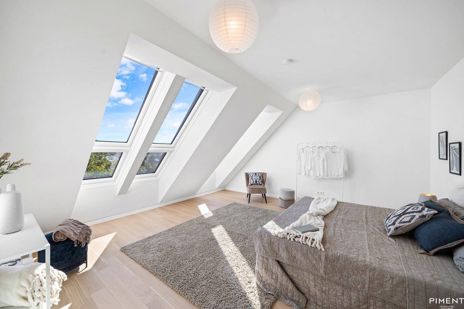 Helles Schlafzimmer im Dachgeschoss mit großen Dachfenstern und Holzboden.
