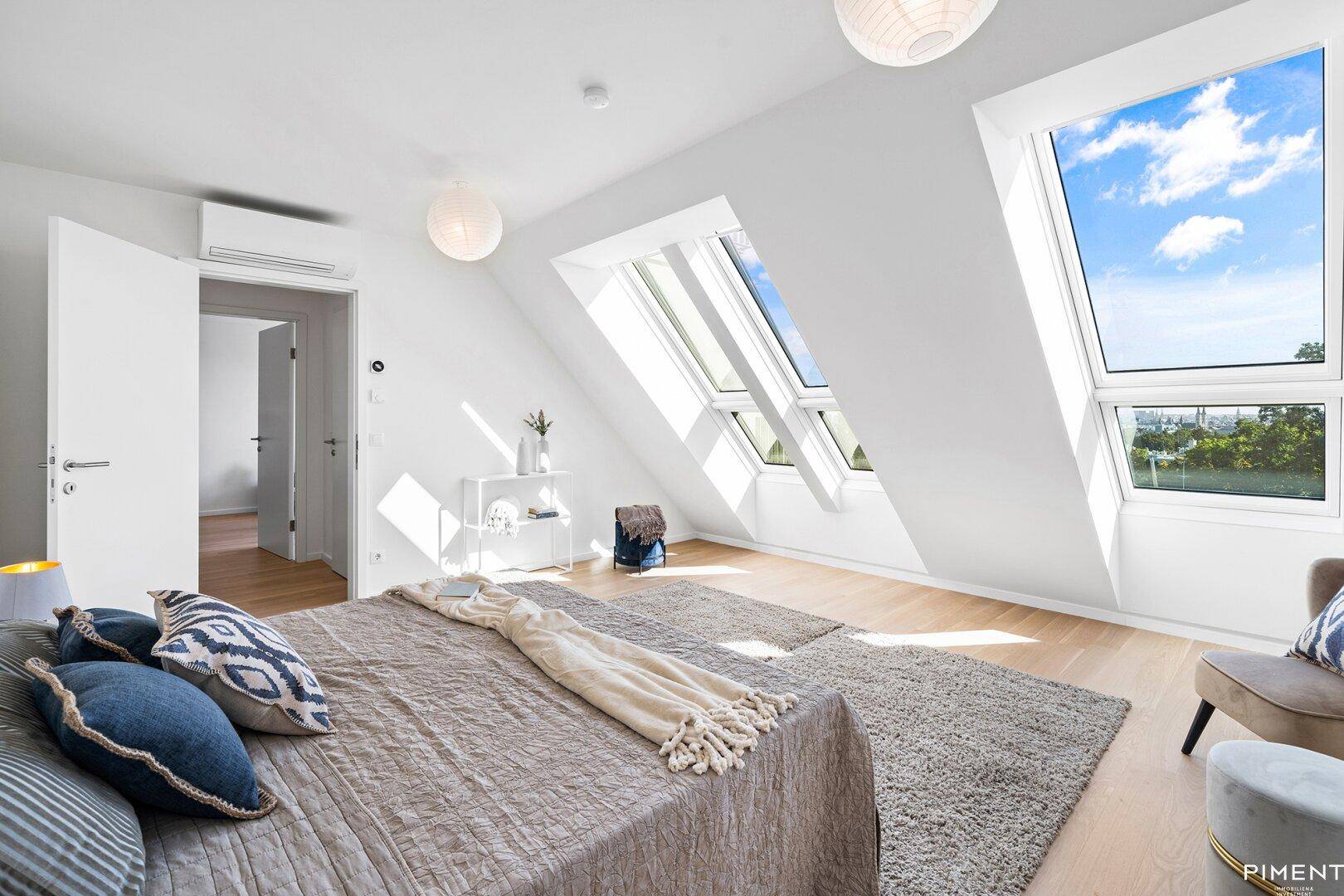 Geräumiges Schlafzimmer mit viel Tageslicht durch große Dachfenster und Zugang zu einem weiteren Raum.