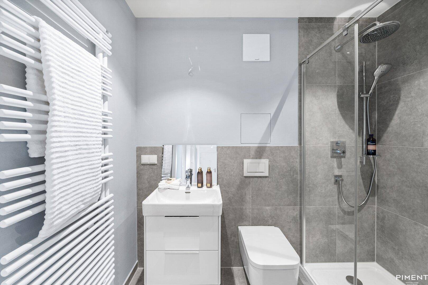Modernes Badezimmer mit Dusche, wandhängendem WC und beheiztem Handtuchhalter.