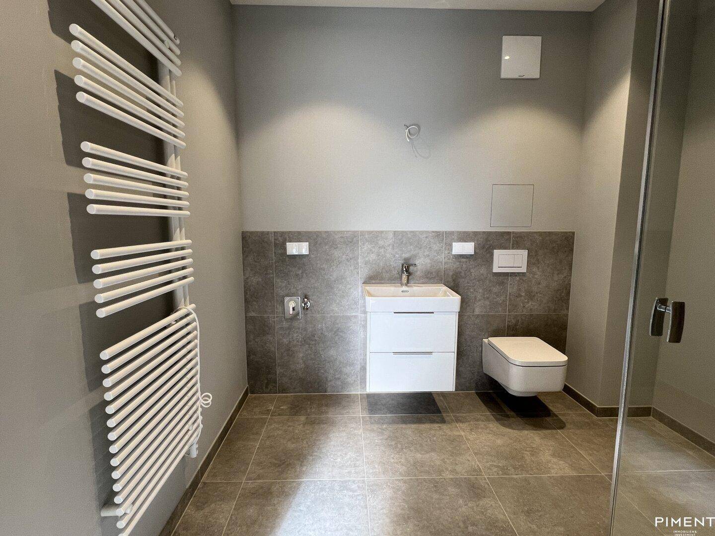Modernes Badezimmer mit grauen Fliesen, Waschtisch, wandhängendem WC und beheiztem Handtuchhalter.