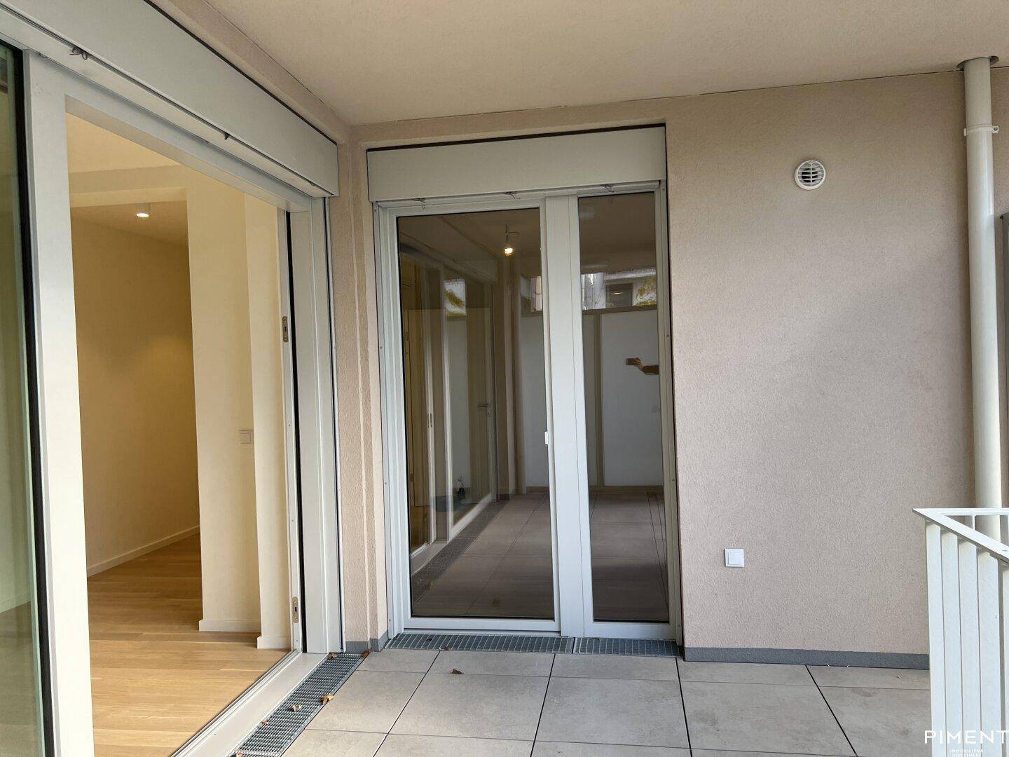 Balkonzugang mit großen Schiebetüren und Außenjalousien, die auf den gefliesten Balkon führen.